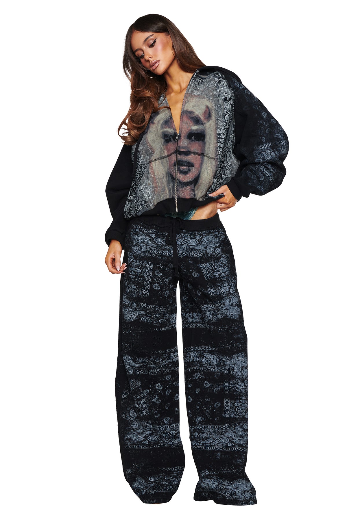 A woman poses in the I.AM.GIA T-REX ZIP THRU HOODIE - BLACK BANDANA, an oversized black hoodie featuring a bold bandana pattern and statement graphic print, effortlessly channeling street style against a plain white background.
