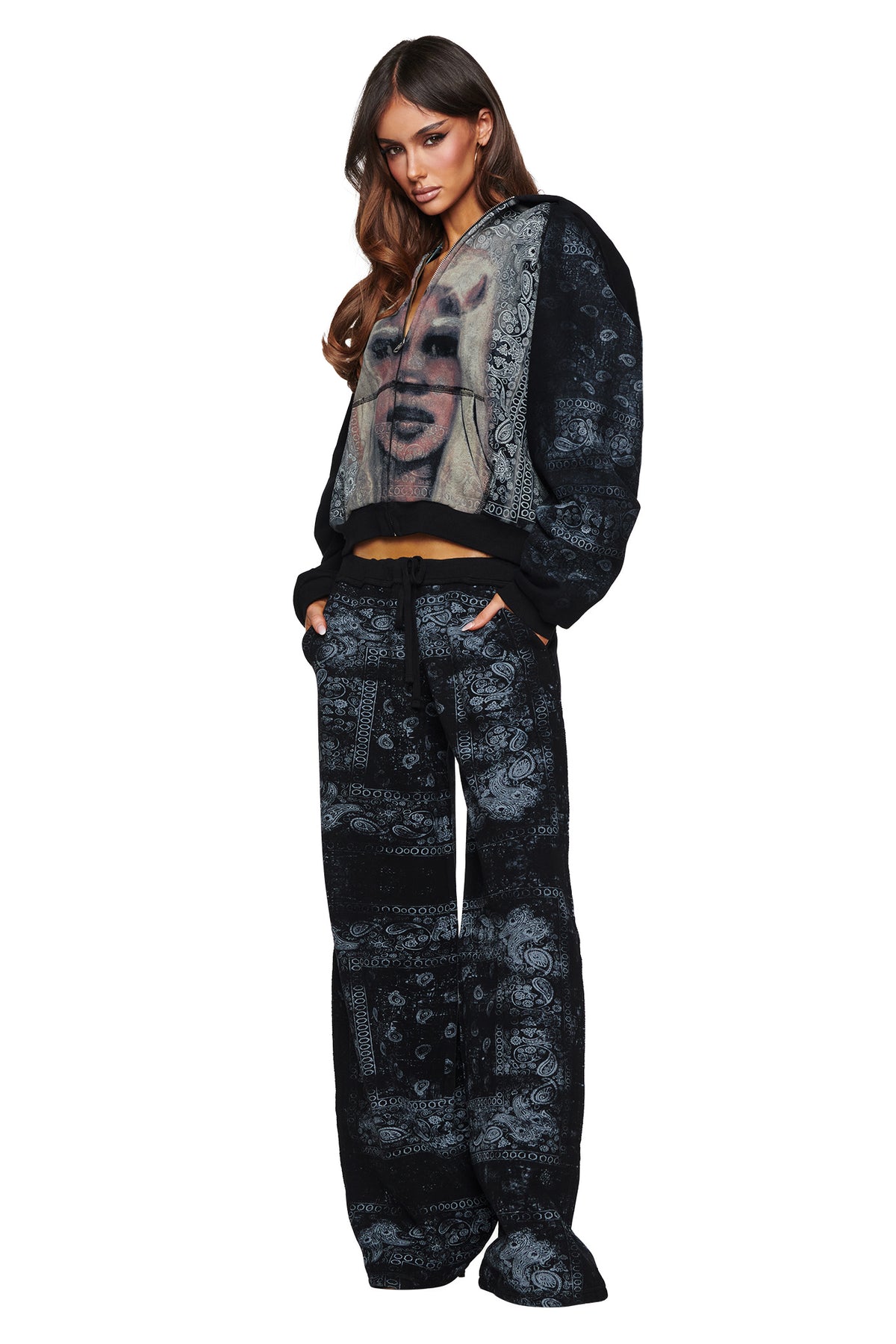 A woman models the I.AM.GIA T-REX TRACKPANT - BLACK BANDANA, featuring wide-leg trackpants and a bold graphic of a woman’s face on the front of the hoodie, standing against a white background and showcasing striking street style.
