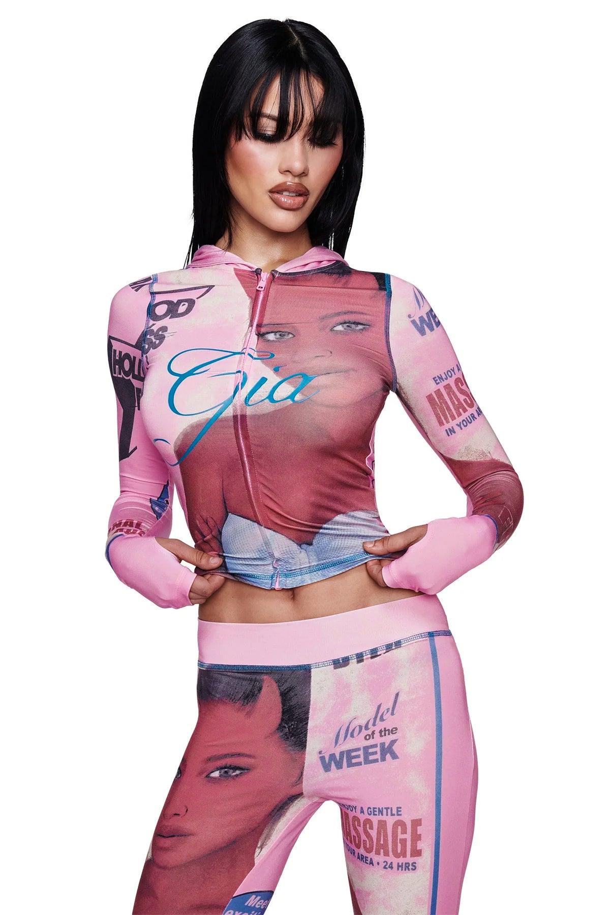 A woman poses in a fitted, pink T-REX BLARE HOODIE by I.AM.GIA, featuring bold, collage-style graphics and retro magazine covers printed across the fabric. She stands with her hands on her hips against a white background.