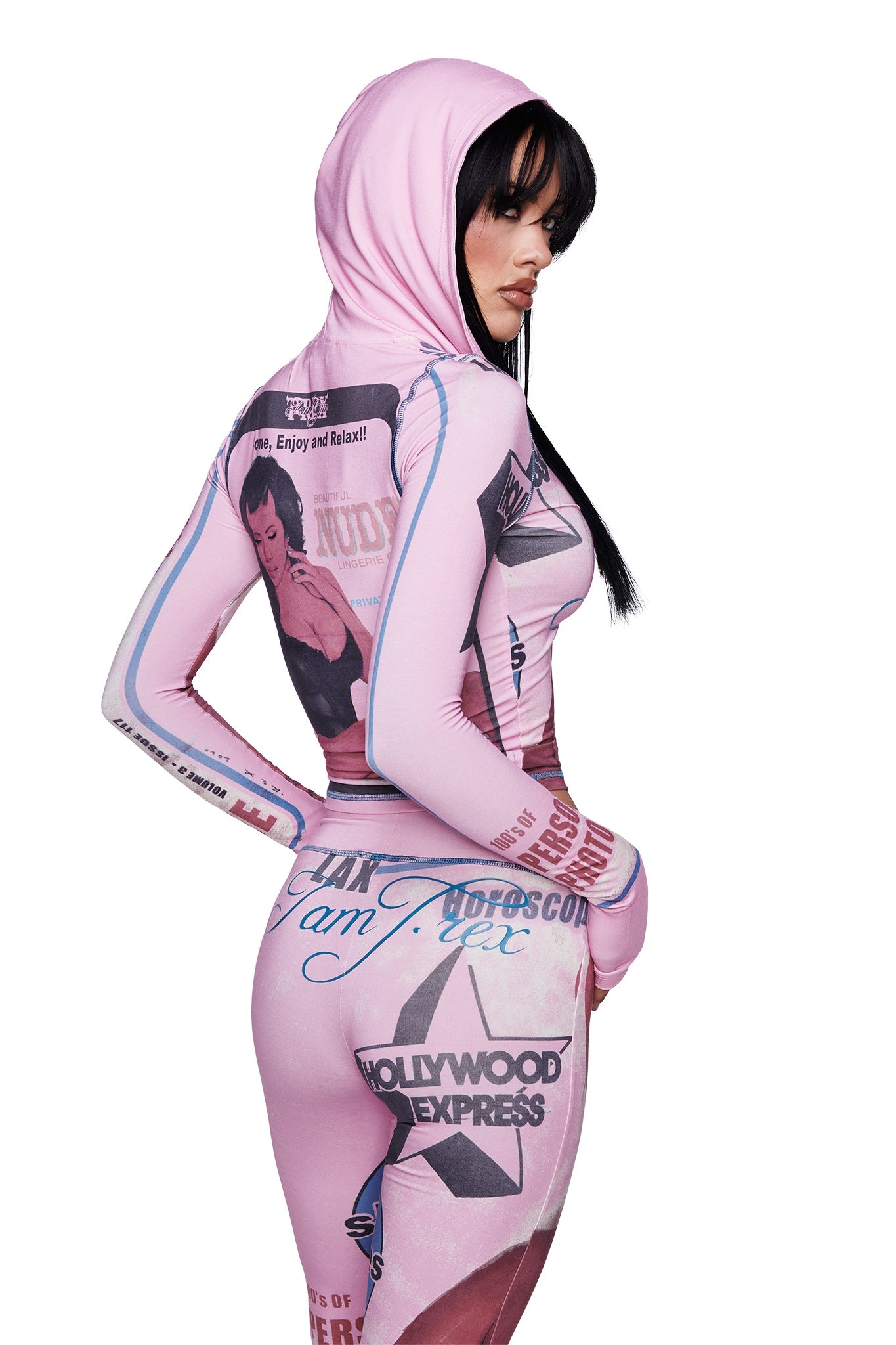 A woman in the I.AM.GIA T-REX BLARE HOODIE - PINK, featuring vintage-style graphic prints, poses sideways with straight black hair and a serious expression, glancing over her shoulder against a white background.