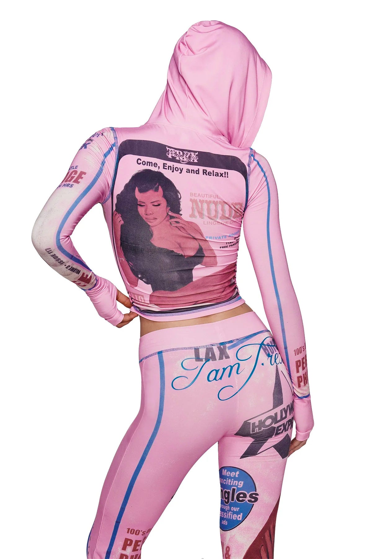 A person wearing the I.AM.GIA T-REX BLARE HOODIE in pink—a bamboo-fabrication hooded outfit—stands with one hand on their hip, facing away. The hoodie features vintage-inspired graphic prints, including a woman's photo and bold text such as “Come, Enjoy and Relax!!” along with various striking words.