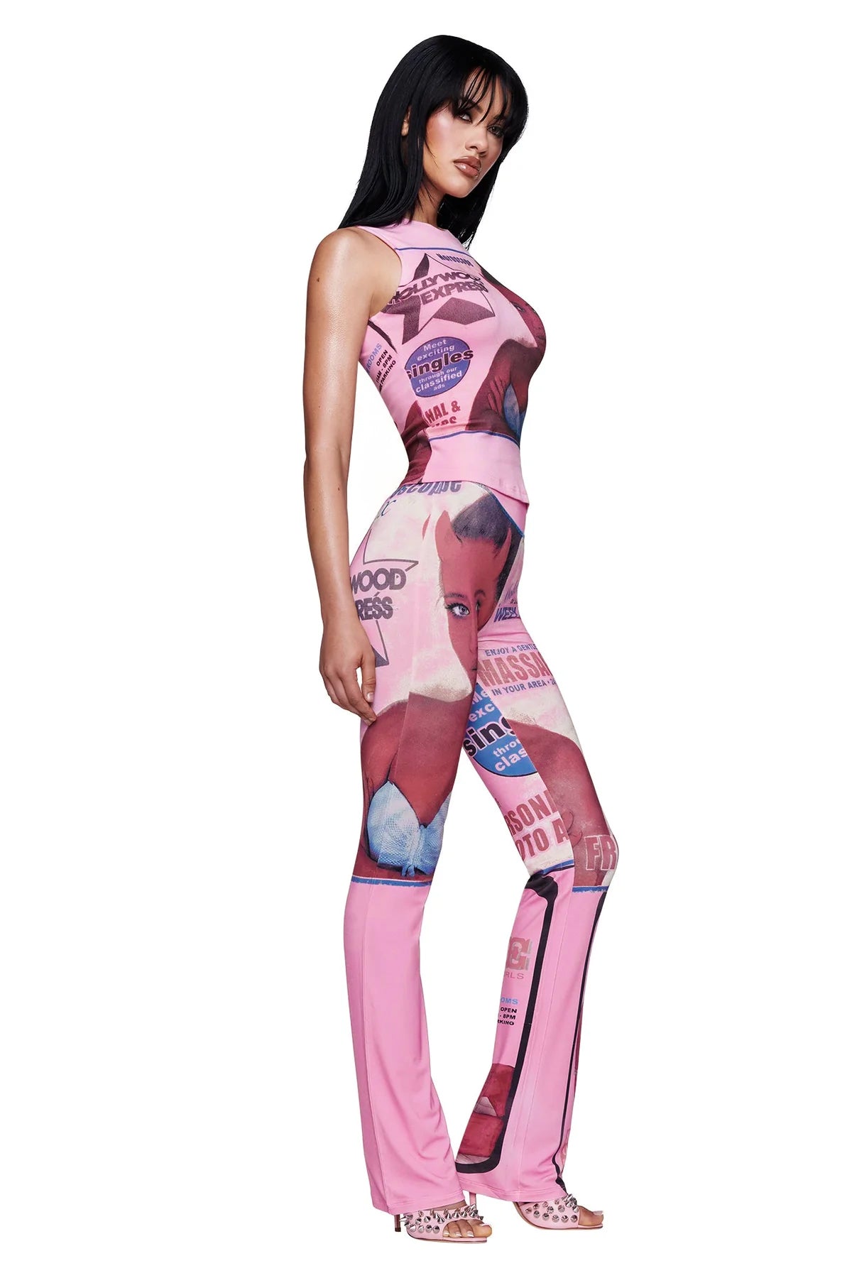 Woman wearing I.AM.GIA T-REX BLARE TRACKPANT in pink with bold graphic collage designs and clear heeled sandals, standing in a side pose against a white background.