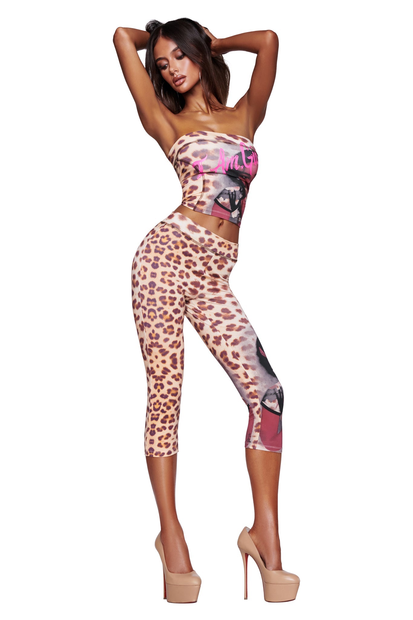 A woman poses confidently with her hands behind her head, wearing the I.AM.GIA T-REX BLARE BOOB TUBE - WILD CARD and matching crop leggings featuring cheetah print and bold graphic accents, set against a white background.