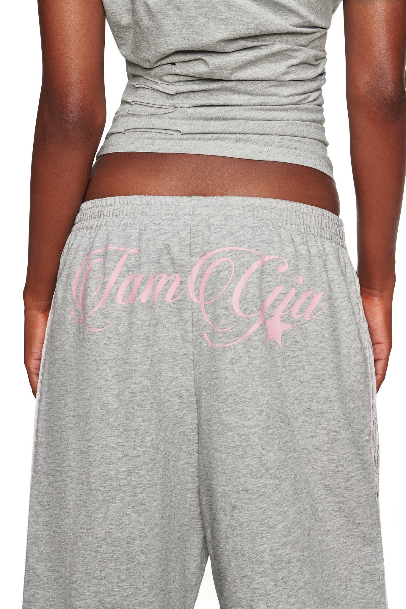 A person wearing the BEX TERRY SHORT in grey by I.AM.GIA, featuring “I am Gia” in pink script across the back and an elasticated waistband for comfort, paired with a matching grey top. The image is cropped to show the lower back and upper legs.