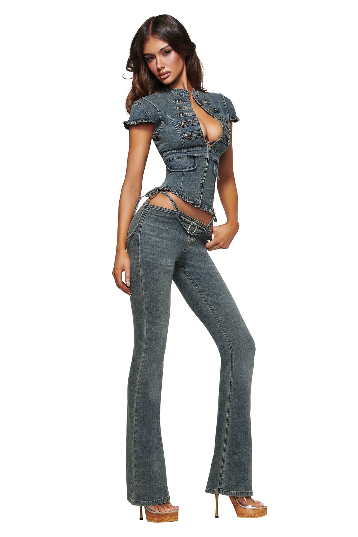 A woman poses confidently against a white background wearing the I.AM.GIA JET DENIM TOP in faded indigo, styled with cutouts and flared pants reminiscent of iconic Y2K fashion, completing the look with high-heeled shoes.