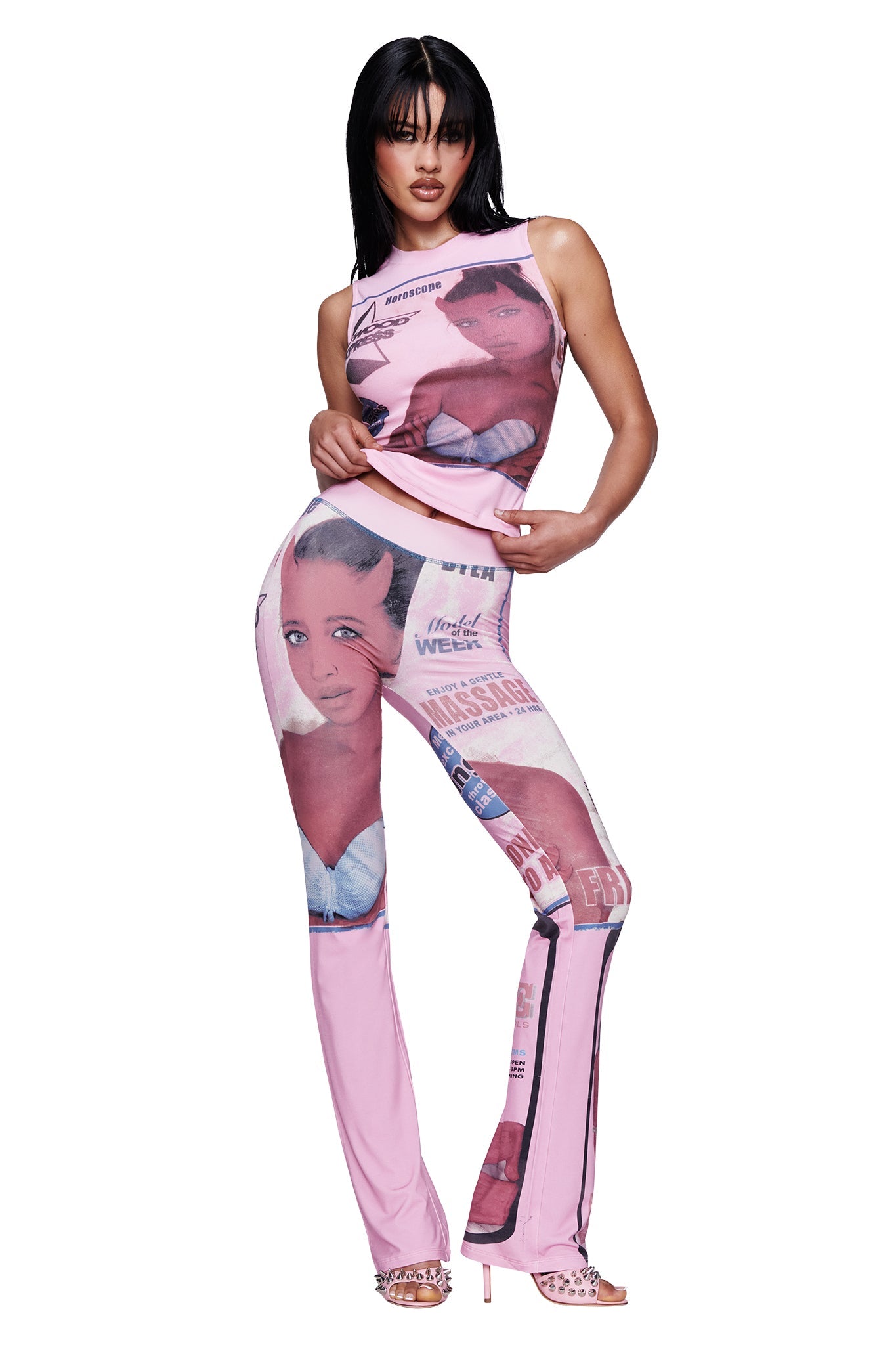 A woman poses against a white background wearing the I.AM.GIA T-REX COURTNEY TANK in pink—a sleeveless muscle tank with magazine-style images and text—paired with matching pants and open-toe heels.