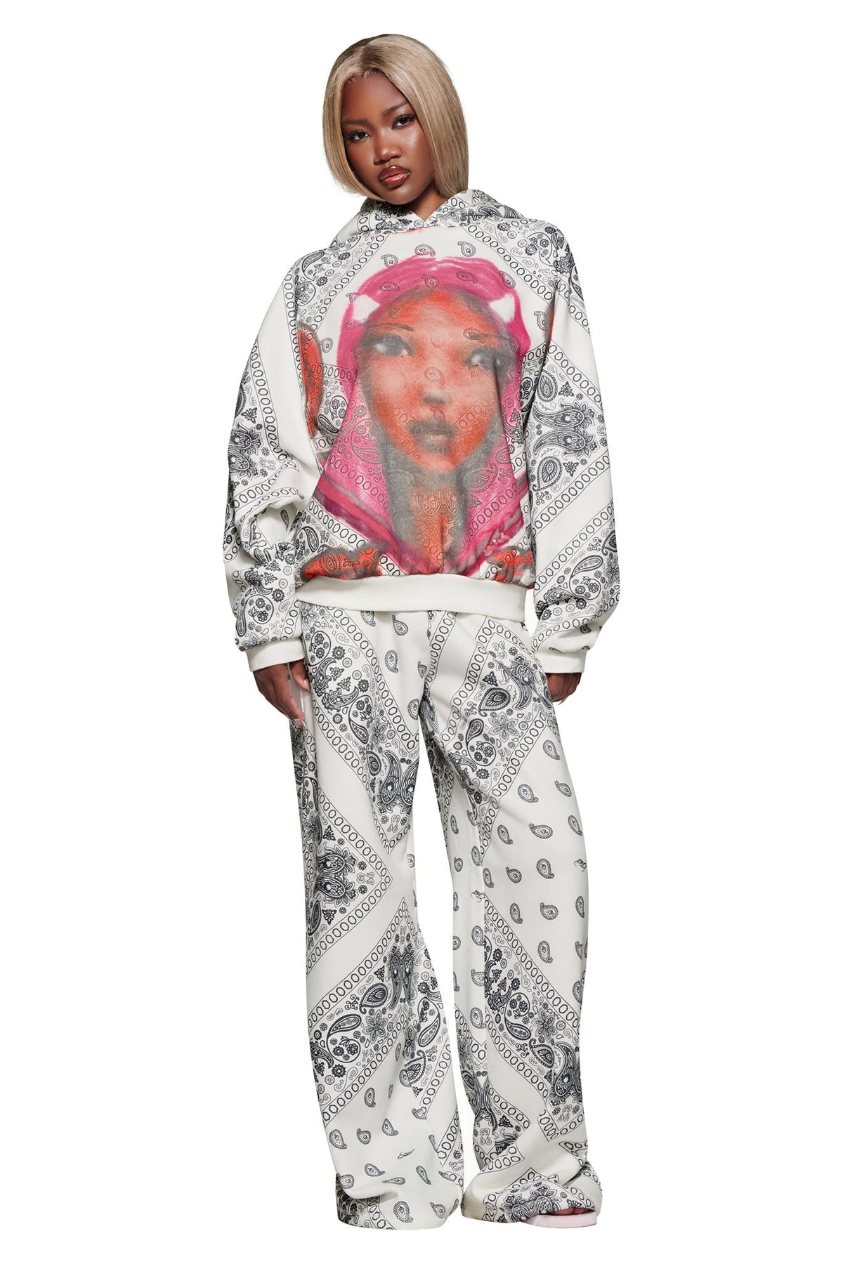 A woman with blonde hair wears the I.AM.GIA T-REX PULLOVER HOODIE - PAISLEY FACE, a white paisley fleece sweatshirt with a large graphic face and pink details, standing against a white background.