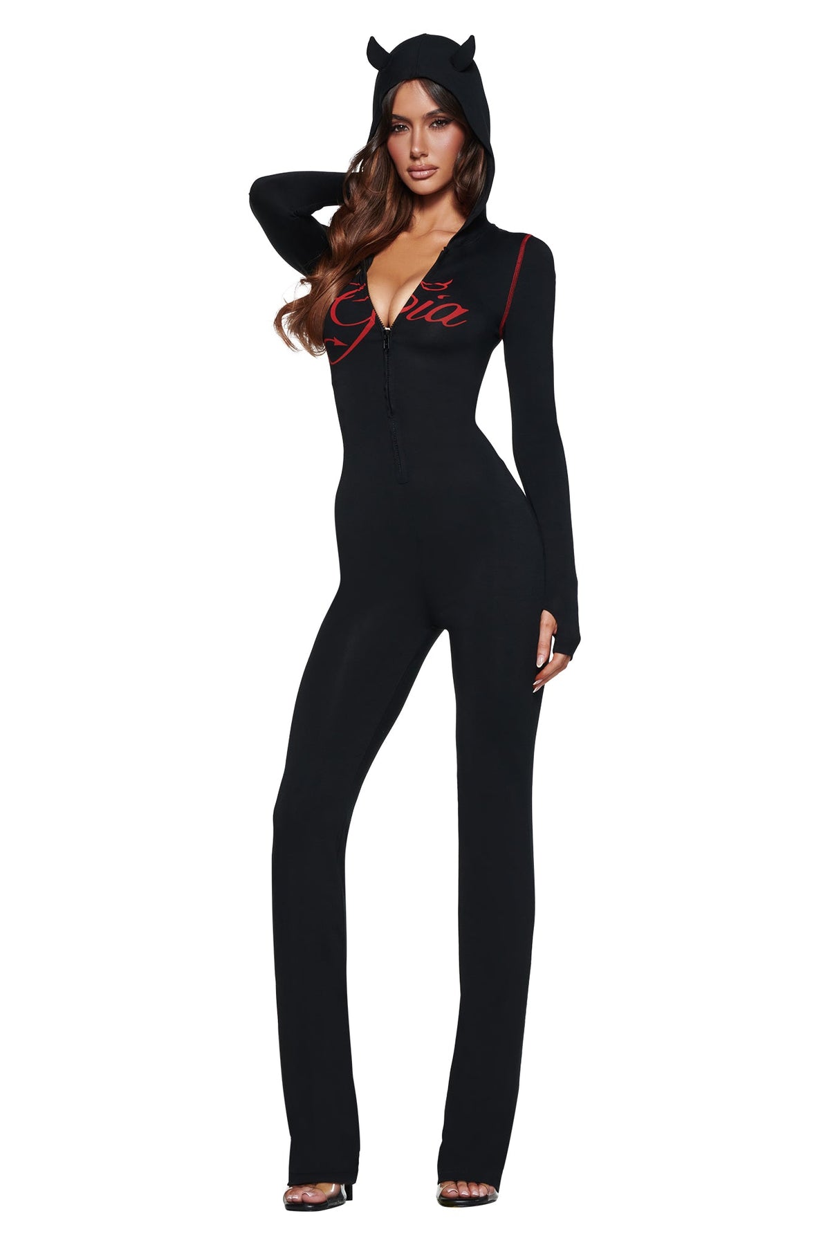 Woman wearing the BLARE HORN JUMPSUIT - BLACK by I.AM.GIA, featuring a devil horn hood and red logo, poses confidently in high heels with one hand on her hip.