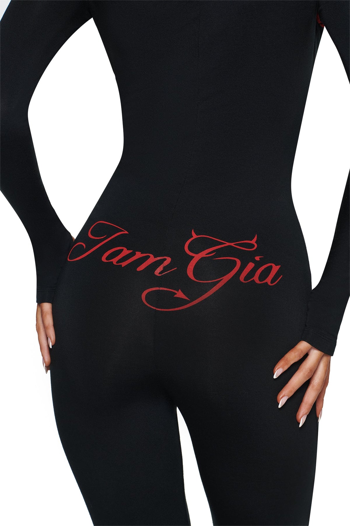 A person wears the BLARE HORN JUMPSUIT - BLACK by I.AM.GIA, featuring a bold red script logo across the back. Only their lower torso and one hand are visible.