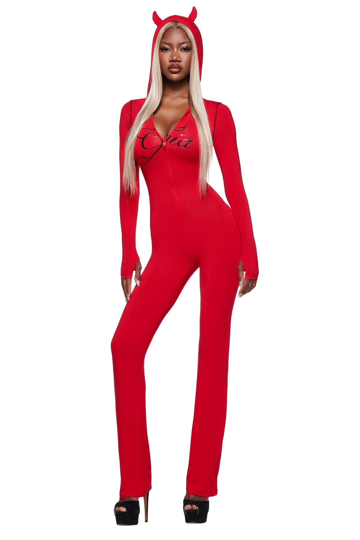 A woman in a BLARE HORN JUMPSUIT - RED by I.AM.GIA, with devil horns, long blonde hair, and black heels, poses confidently against a white background.
