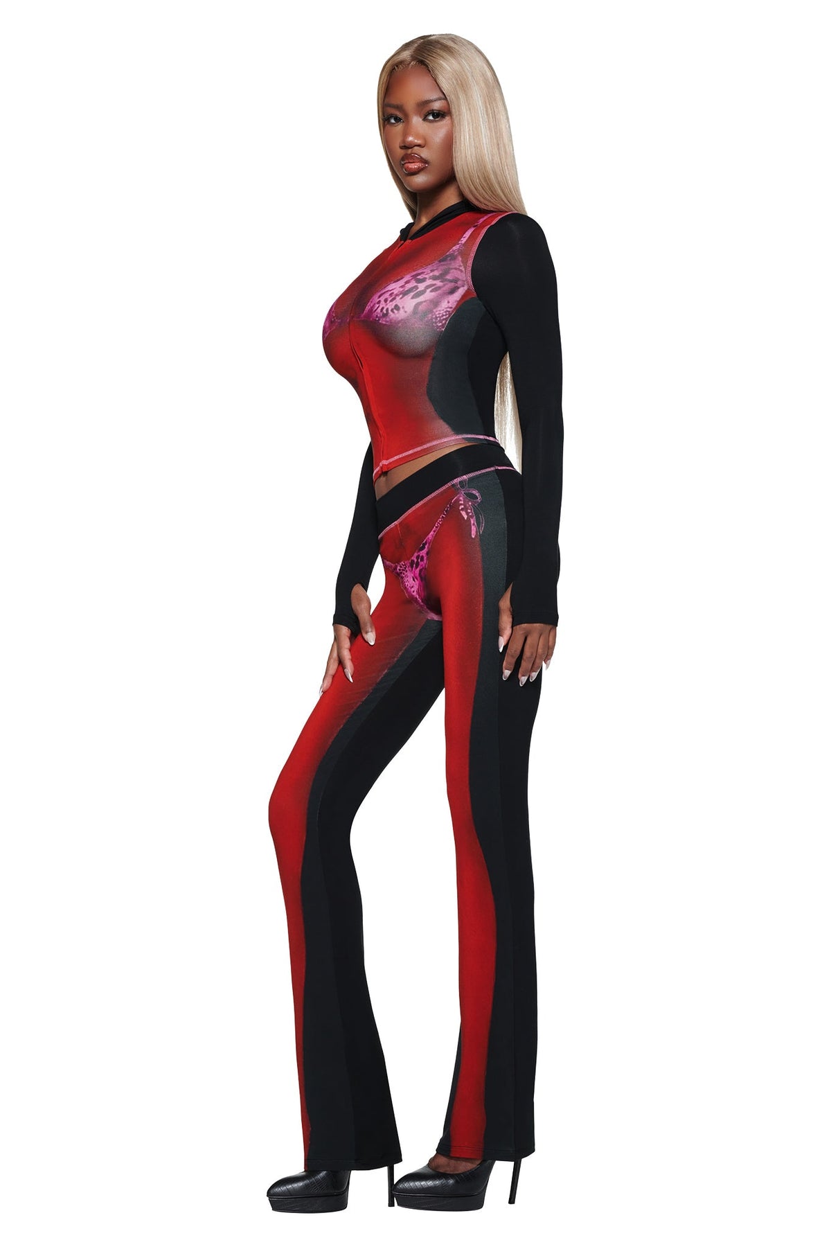 Woman with long blonde hair in the I.AM.GIA T-REX SPRAY BODY BLARE HOODIE - BLACK, standing in profile on high heels against a white background.