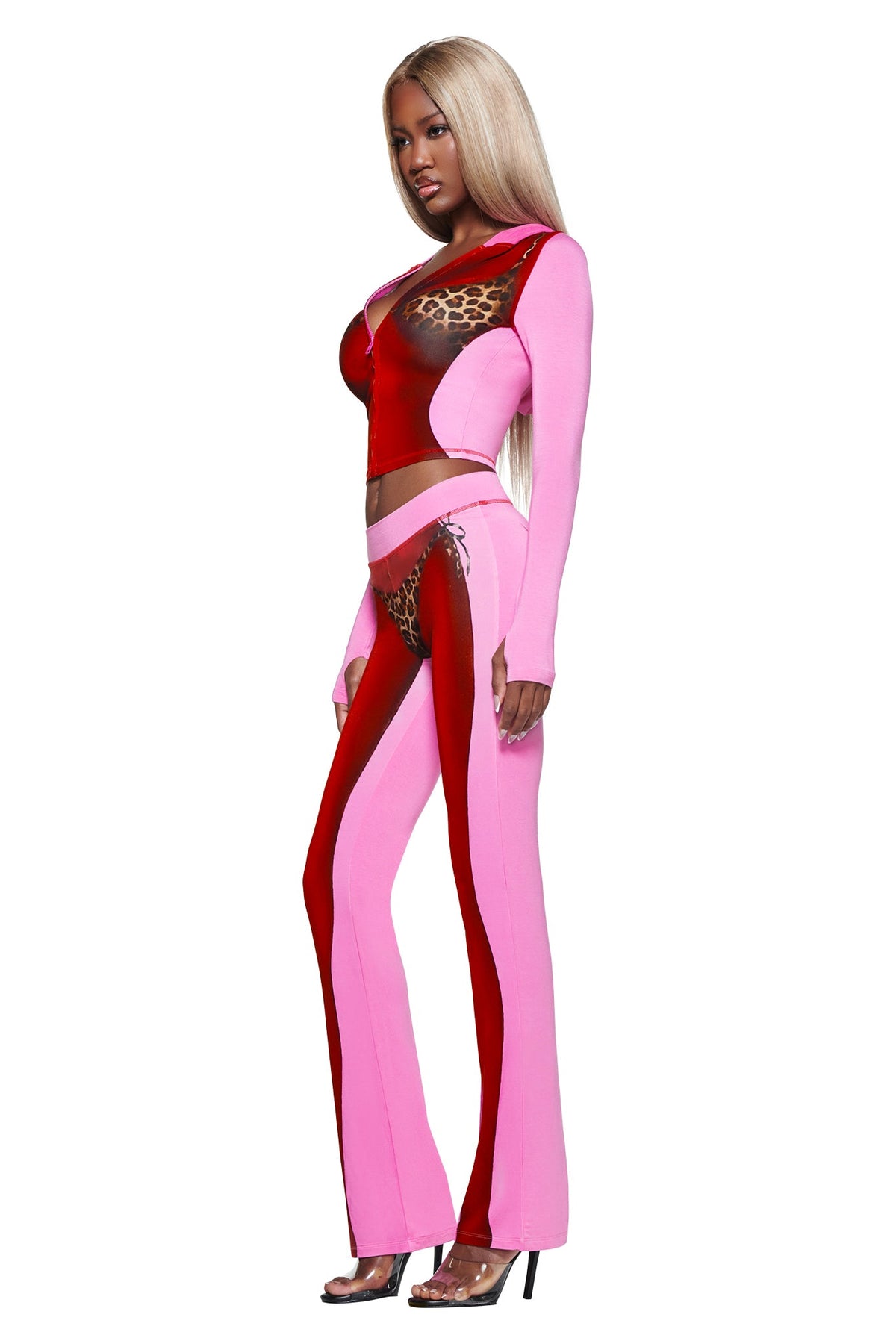 A woman with long blonde hair wears the I.AM.GIA T-REX SPRAY BODY BLARE HOODIE - PINK, featuring a fitted design with airbrushed bikini print and leopard accents, standing in high heels against a white background.
