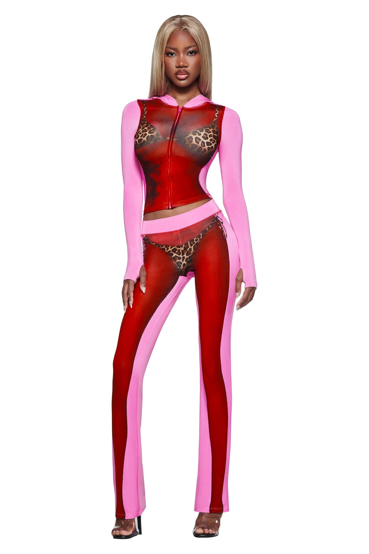 A woman models the I.AM.GIA T-REX SPRAY BODY BLARE TRACKPANT - PINK, revealing leopard print bra and underwear beneath sheer red and pink panels. She has long blonde hair and wears high heels.