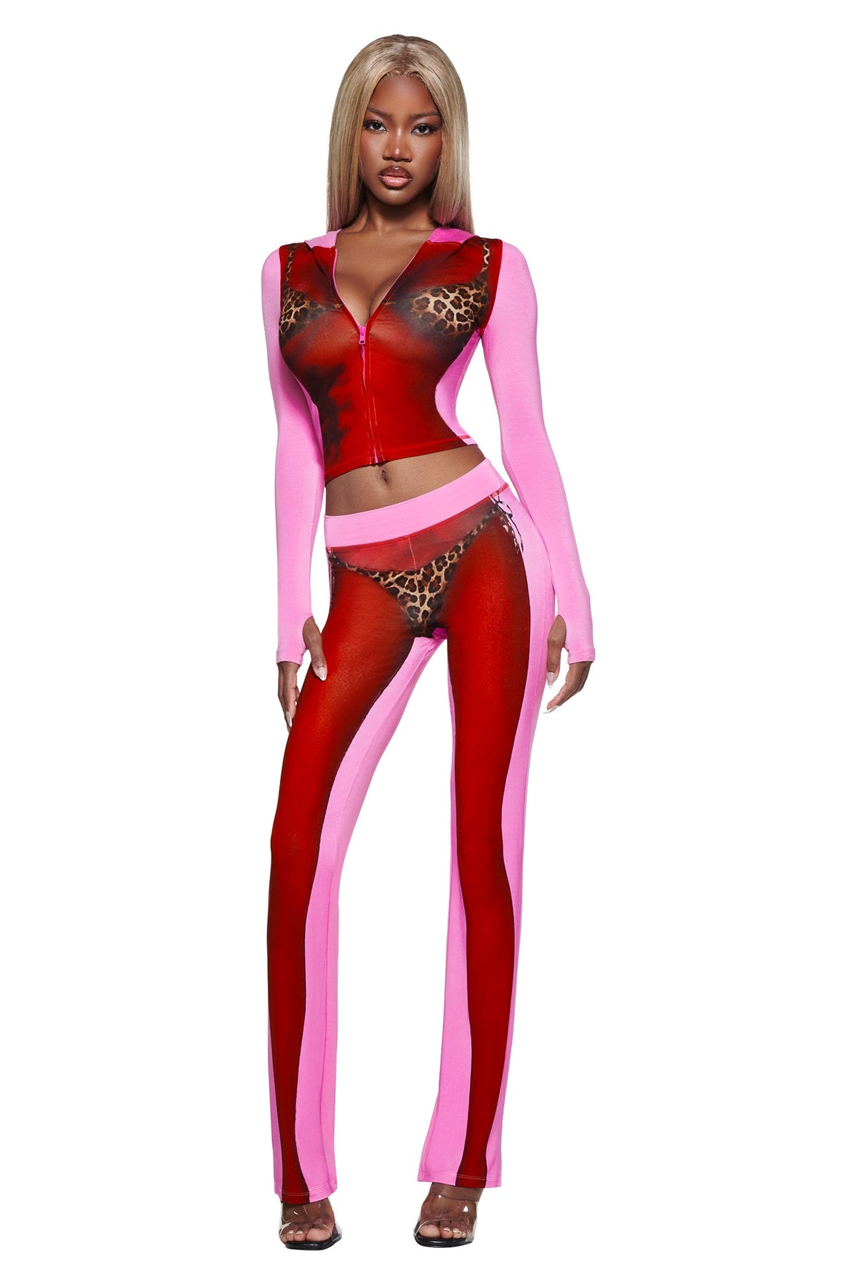 Woman wearing the T-REX SPRAY BODY BLARE TRACKPANT - PINK by I.AM.GIA, a bright pink and red leopard print two-piece with sheer panels, poses in high heels against a white background.