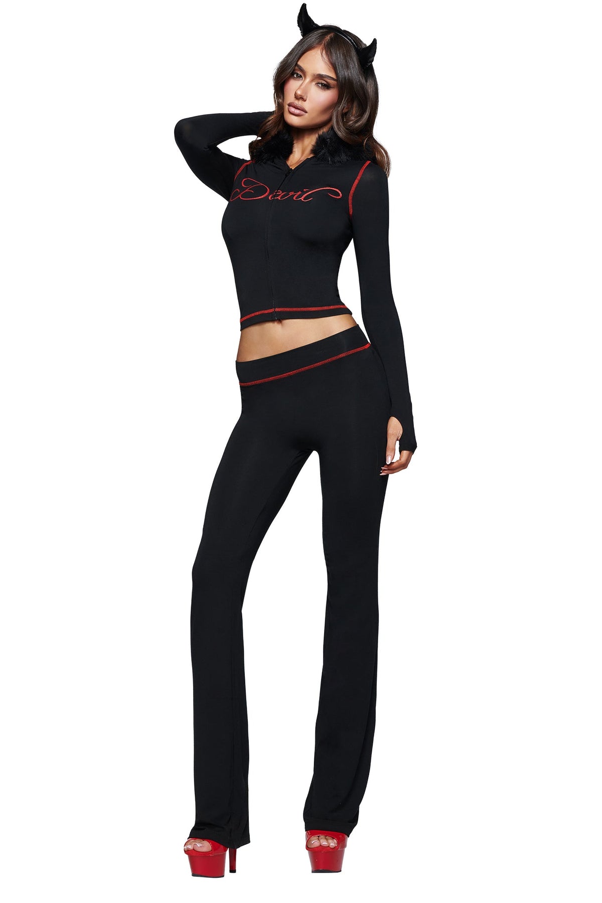A woman wearing the I.AM.GIA BLARE FUR TRIM HOODIE in black, styled with red accents, bold red platform heels, and a black devil horns headband. The sleek hoodie features fur trim detailing and “Devil” written across the front in striking red script. She poses confidently with one hand resting on her head.