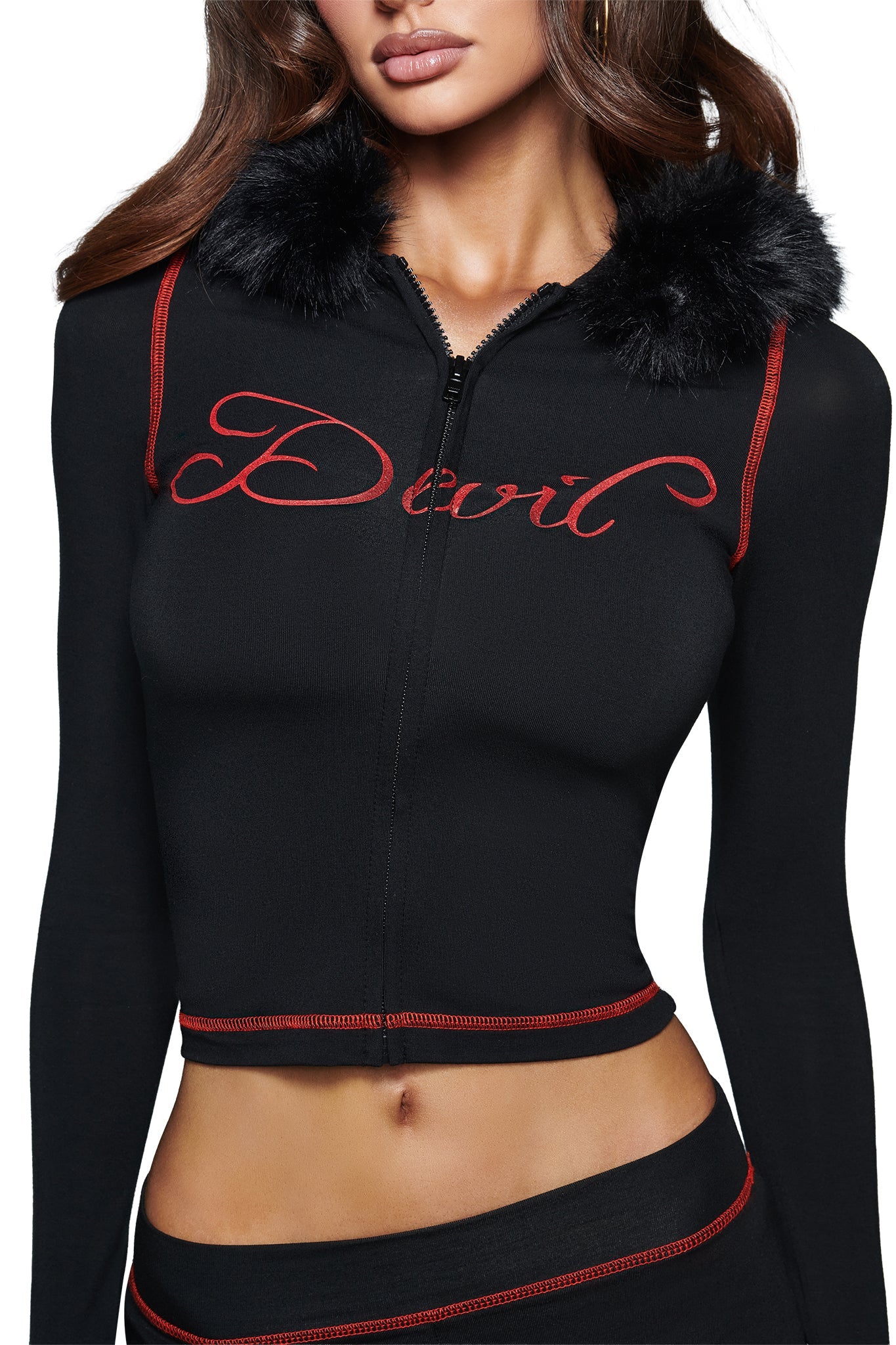 A woman models the I.AM.GIA BLARE FUR TRIM HOODIE in black, showcasing its red trim, faux fur collar, and bold cursive “Devil” graphic on the front. Her partially visible face accentuates the edgy vibe of this standout hoodie.