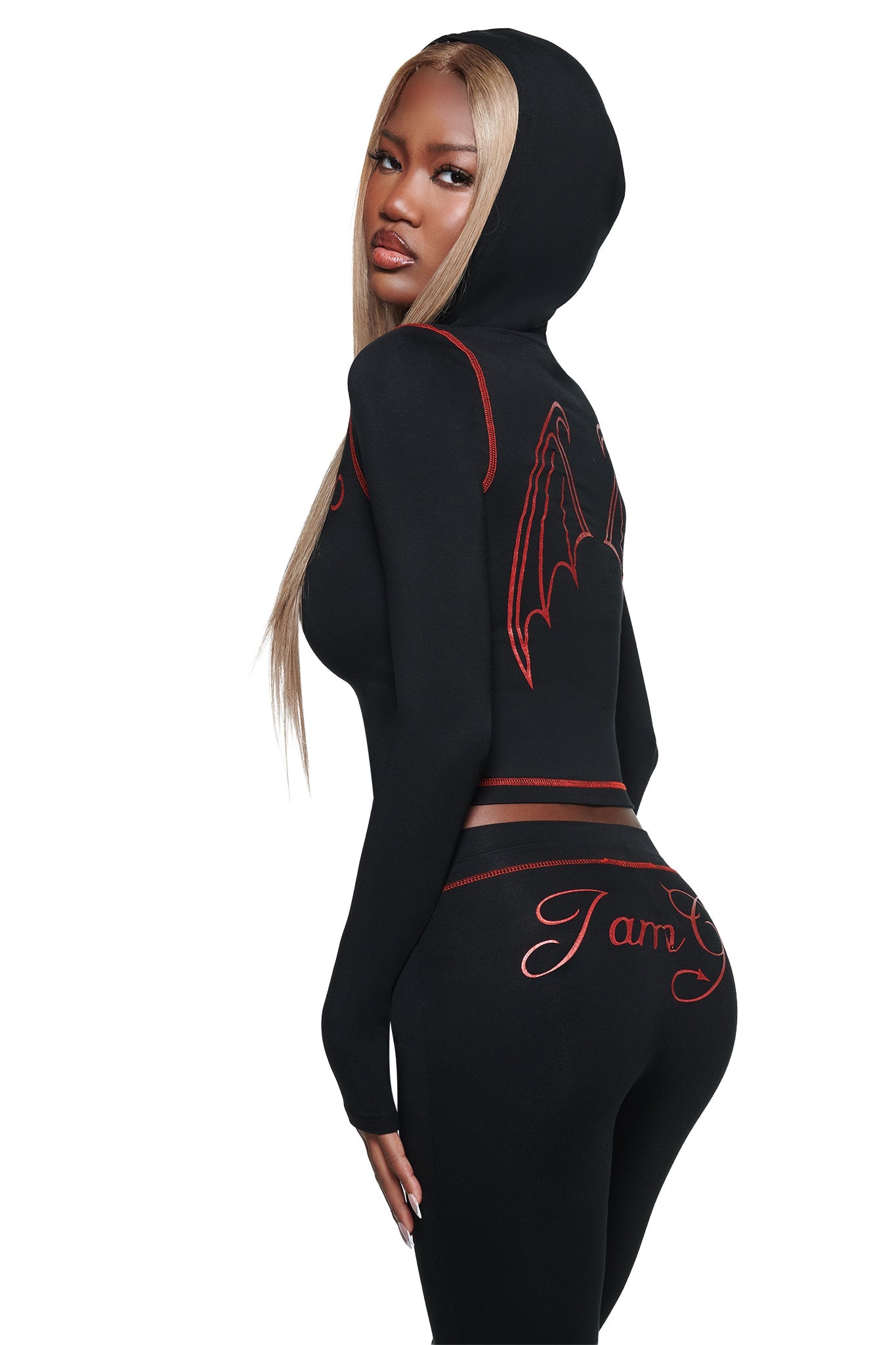 A woman poses looking over her shoulder against a white background, showcasing the I.AM.GIA BLARE FUR TRIM HOODIE in black, a fitted hoodie with red stitching and a striking bat-wing design on the back.