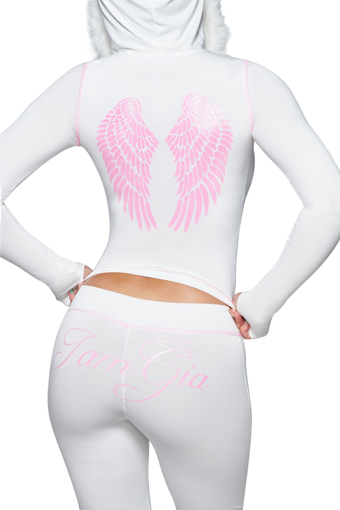 A person is photographed from behind against a white background, wearing the I.AM.GIA BLARE TRACKPANT - WHITE : ANGEL, which features pink angel wings on the back and “I.AM.GIA” in cursive on the low-rise waist, paired with a white outfit.