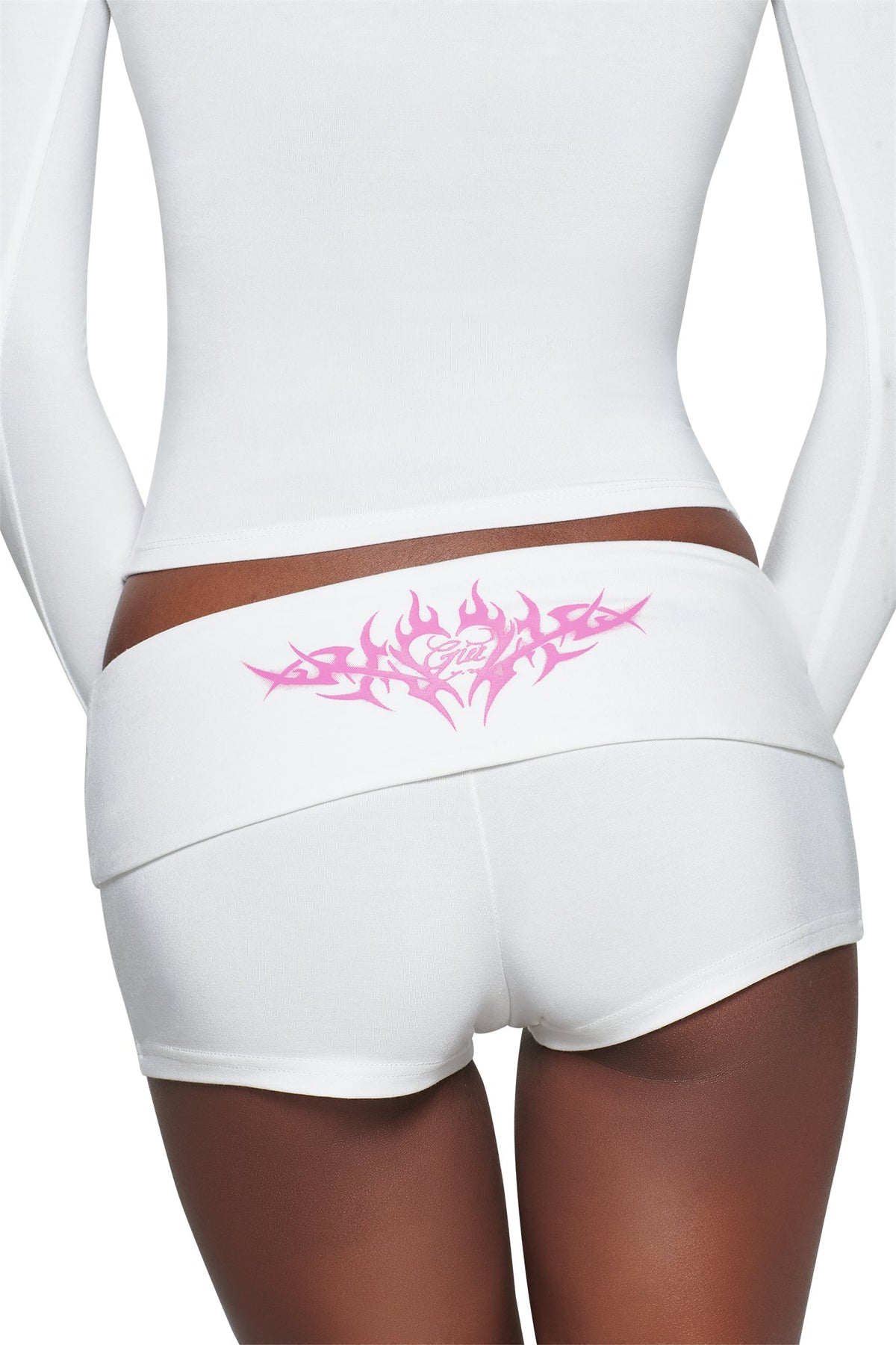 A person wearing I.AM.GIA T-REX BLARE 2.0 SHORT - WHITE featuring a pink tribal graphic on the foldover waistband and a long-sleeve top, seen from behind.