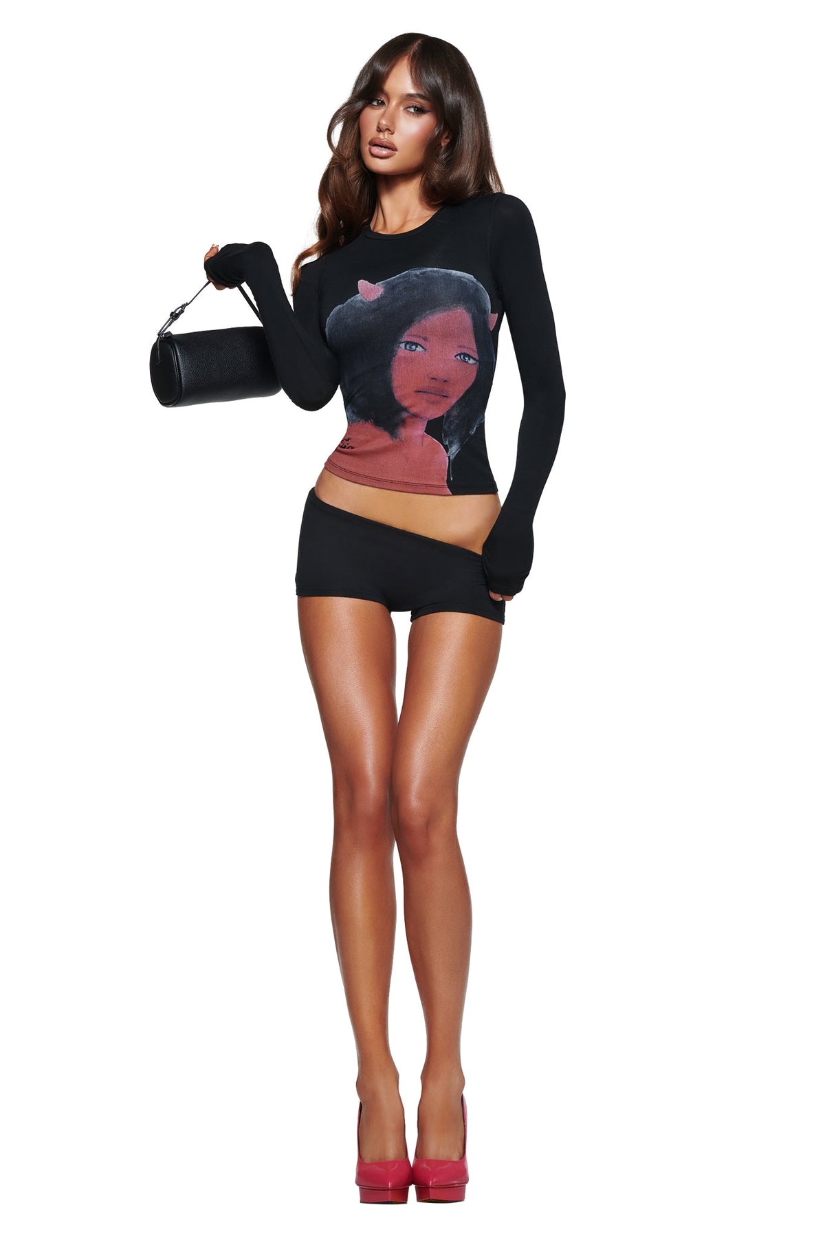 Woman wearing the T-REX BLARE 2.0 SHORT - BLACK by I.AM.GIA, styled with a black long-sleeve graphic top, pink heels, and a small black handbag against a white background.