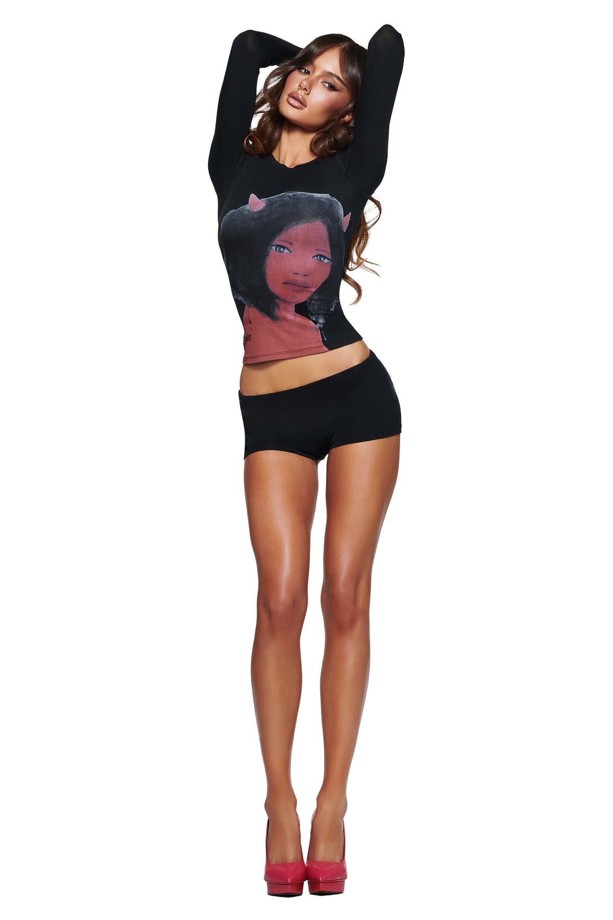 Woman posing with arms raised, wearing I.AM.GIA T-REX BLARE 2.0 SHORT - BLACK, a long-sleeve black graphic top, and red heels against a white background.