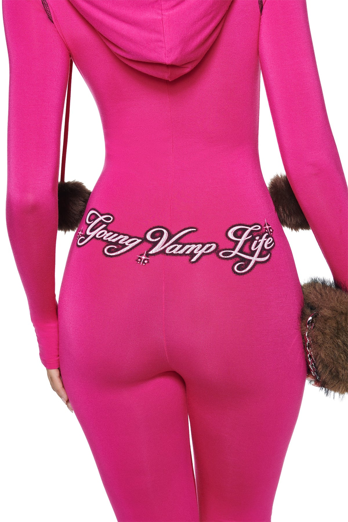 Bright pink I.AM.GIA YVL BLARE FUR LINED JUMPSUIT - PINK with a faux fur hood, featuring brown faux fur trim at the sleeves and waist and the embroidered text “Young Vamp Life” across the back.