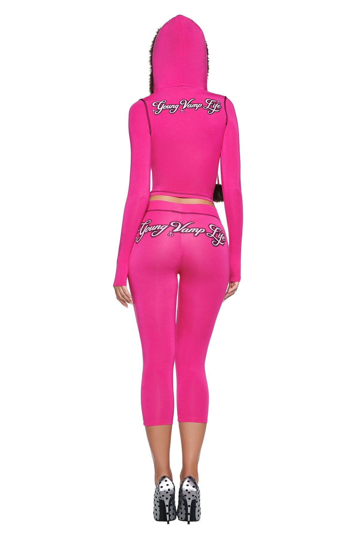 A woman seen from behind wearing a pink YVL BLARE FUR LINED HOODIE and matching leggings, both featuring the text “Young Vamp Life” in cursive.
