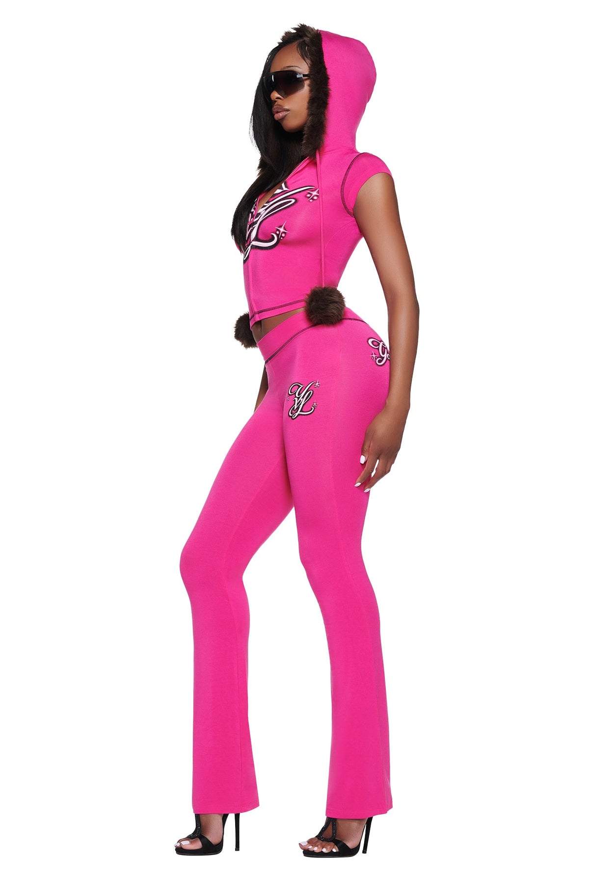 A person wearing a bright pink hooded short-sleeve top and matching YVL BLARE TRACKPANT - PINK with fur-trimmed details and graphic lettering.