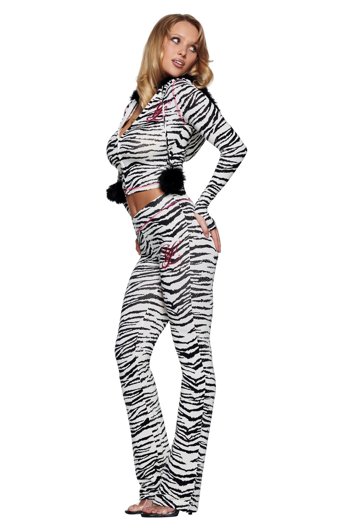 A woman models a matching white and black zebra-print hooded track jacket and flared-leg YVL BLARE TRACKPANT - ZEBRA with black pom-pom accents.