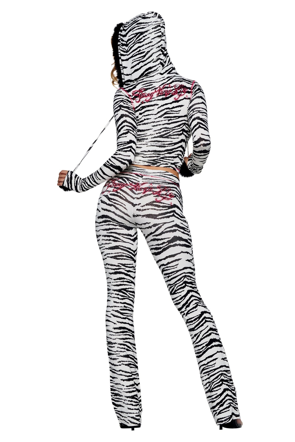 A person seen from behind wears a white and black zebra-print hooded long-sleeve top and matching YVL BLARE TRACKPANT - ZEBRA with flared legs, featuring pink cursive embroidery.