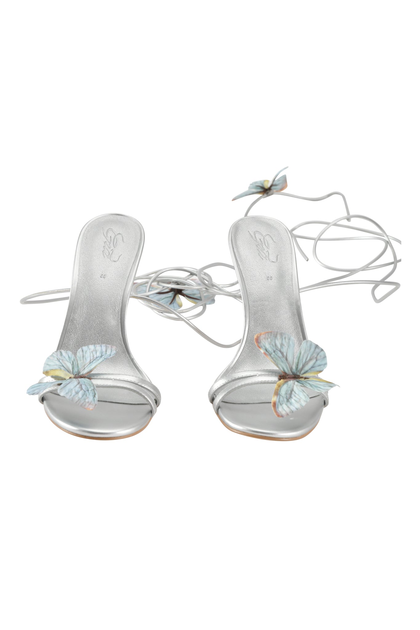 The SCARLETTE HEEL - SILVER by I.AM.GIA features metallic silver strappy stilettos with thin ankle straps and a decorative blue butterfly applique on the open toe, shown against a white background.
