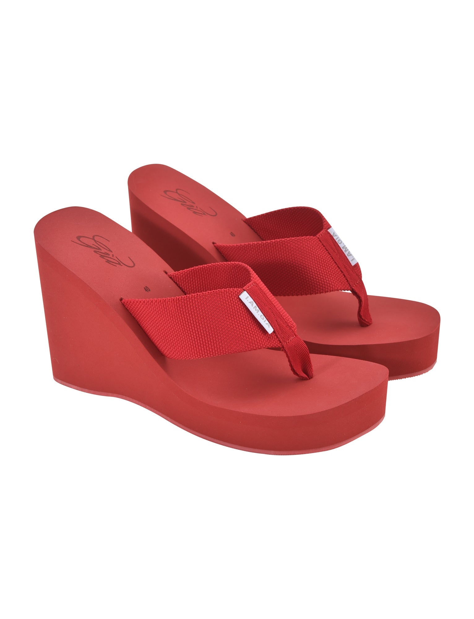 A pair of red SHELBY FLIP FLOP sandals from I.AM.GIA featuring thick soles and wide fabric straps. These wedge flip-flops boast a high platform heel and a thong-style design, with small I.AM.GIA labels on the straps adding a stylish touch to the bright red footwear.