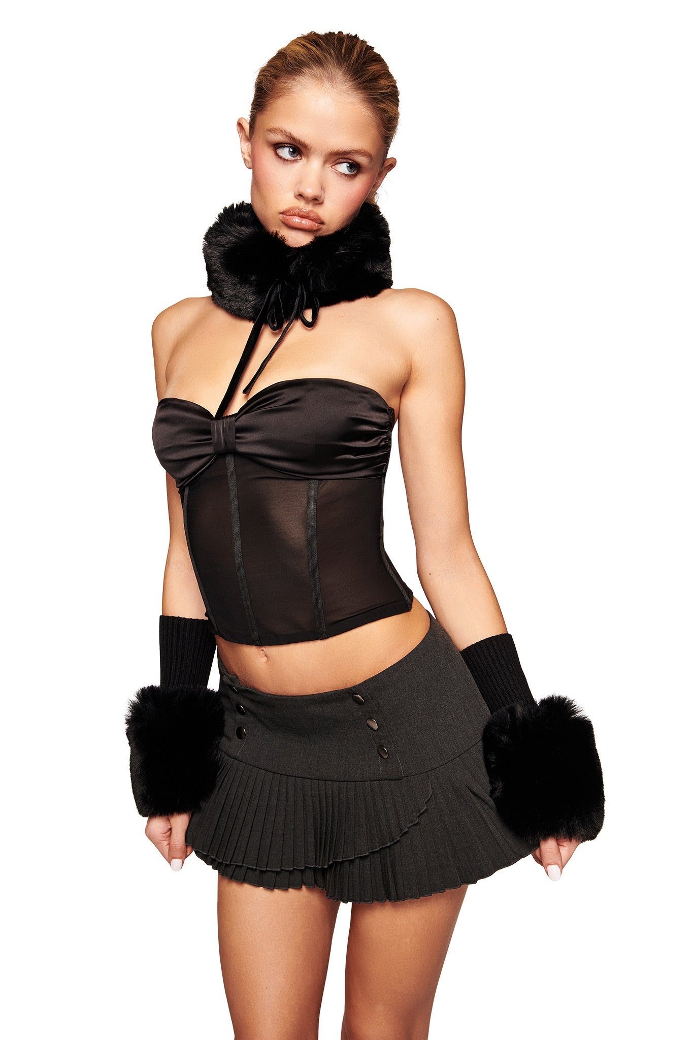 A woman wearing the I.AM.GIA DENALI FUR RIB CUFF in black, paired with a black strapless corset top, pleated mini skirt, and matching fur choker, stands against a white background looking off to the side with a neutral expression.