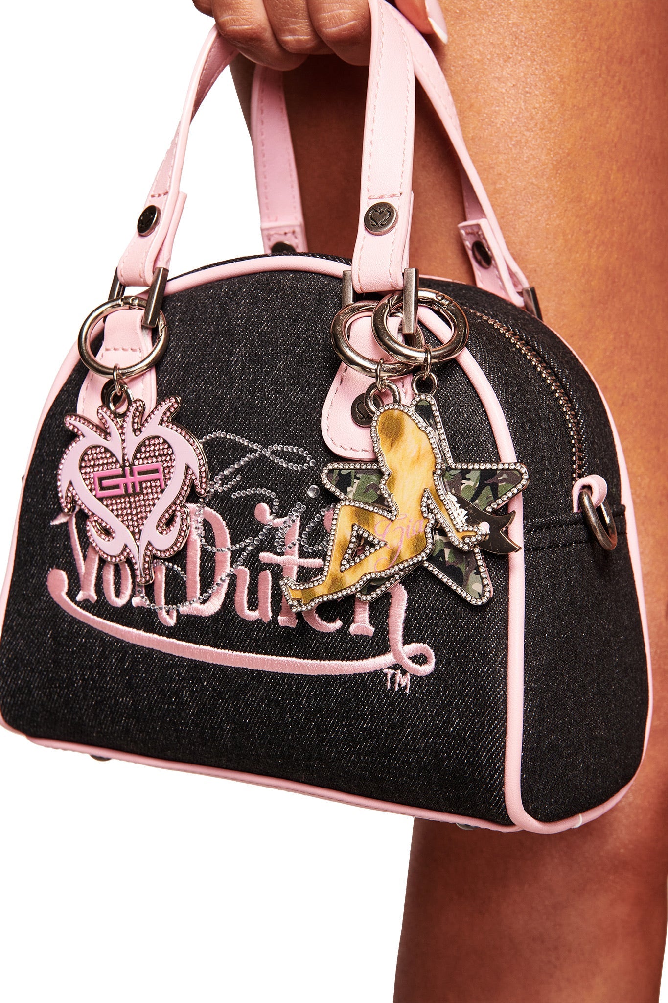 A hand holds the I.AM.GIA X VON DUTCH GIRL KEYCHAIN - LEOPARD PINK GIRL, a chic black and pink bag charm from I.AM.GIA, perfect for adding Y2K style to any look.