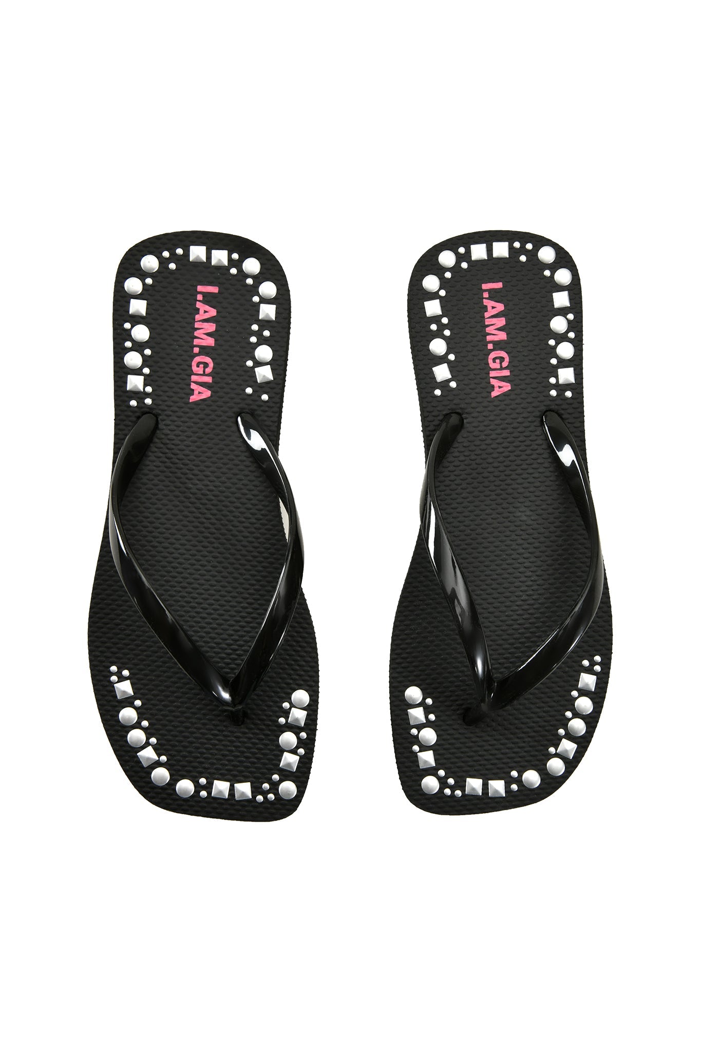 The INKA STUDDED FLIP FLOP by I.AM.GIA features black flip flops with white circular and square studs along the edges, an extra-soft foam footbed, and "LAMIGA" in pink on the footbeds.