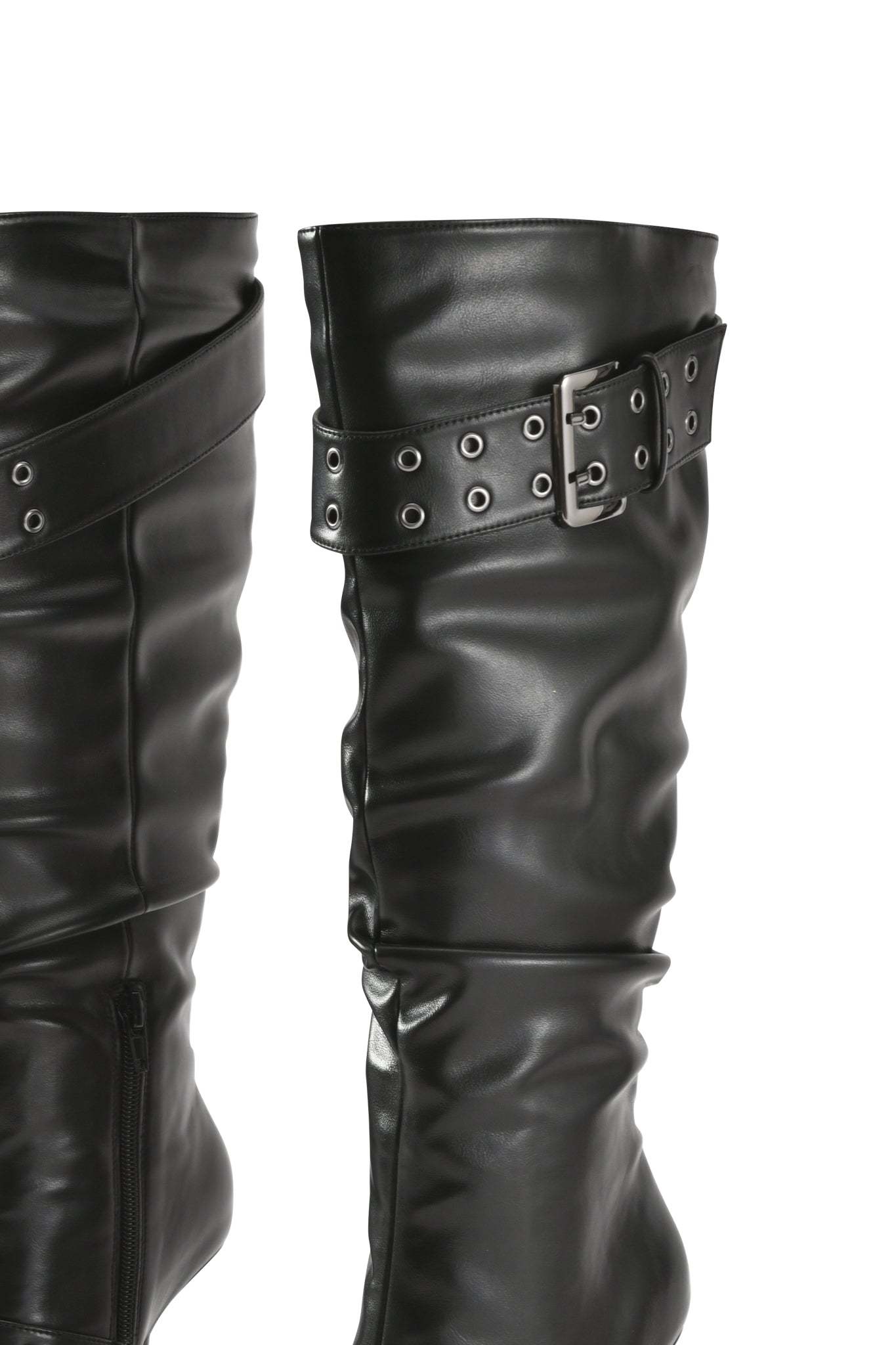 Close-up of the I.AM.GIA KINTH BOOT 2.0 in black, a knee-high faux-leather boot featuring a decorative harness buckle strap and silver eyelets, shown against a white background.