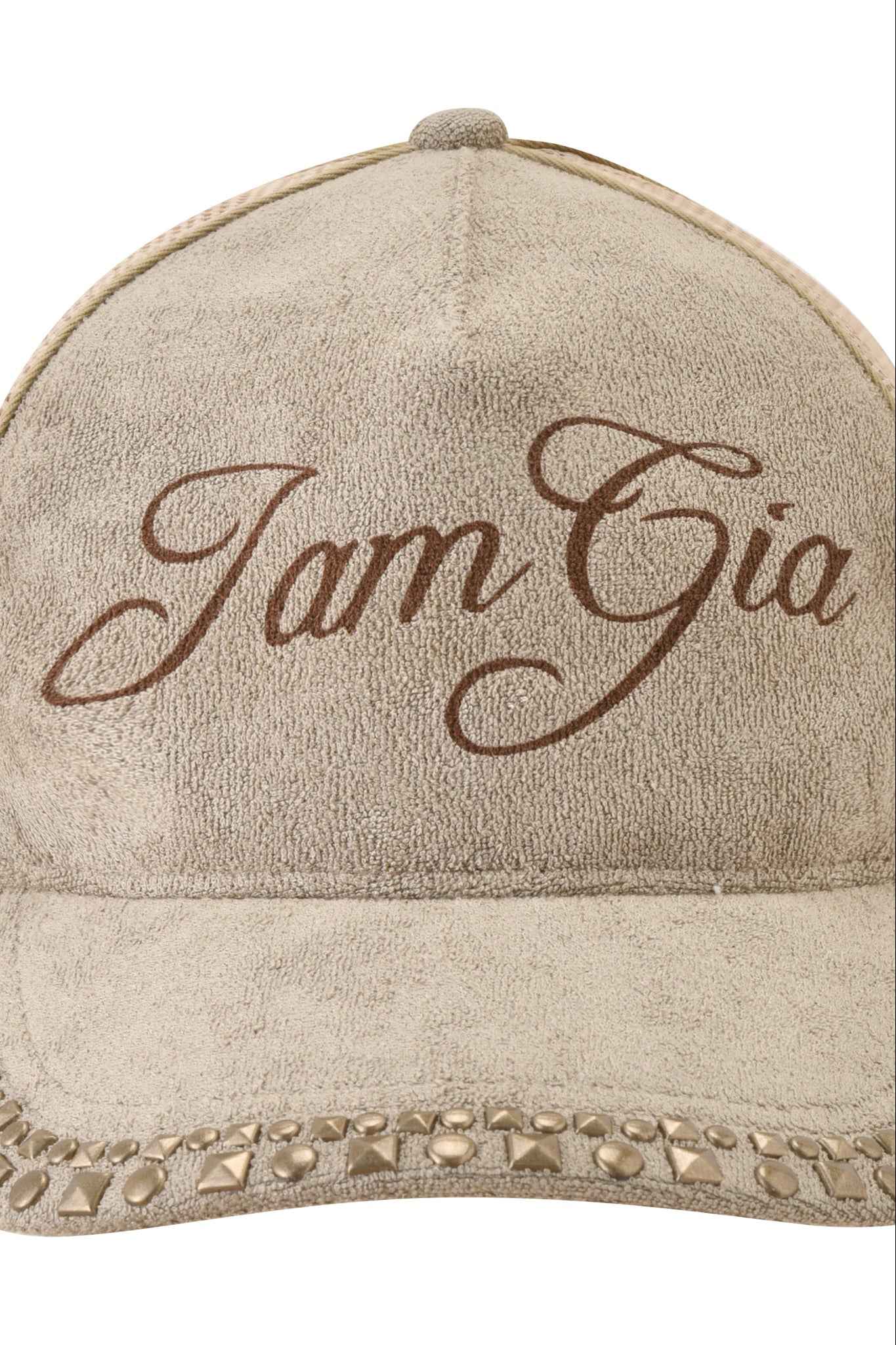 The ISSHA TERRY HAT - STONE by I.AM.GIA is a beige suede snapback trucker hat with "I am Gia" in brown cursive on the front and a brim embellished with metal studs and pyramid accents for a distinctive look.