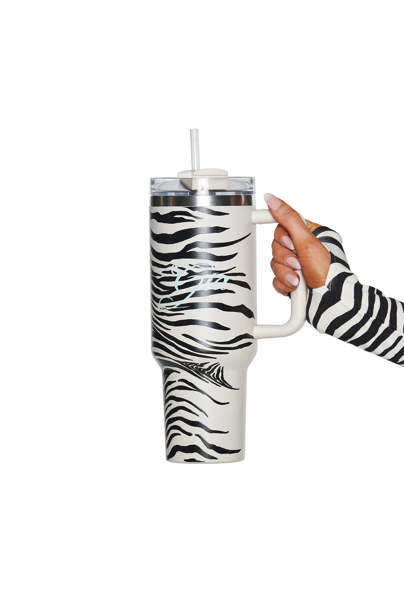 A hand wearing a zebra-striped sleeve holds the I.AM.GIA BLARE CUP - FINE LINE ZEBRA, an insulated stainless steel tumbler featuring a matching black and white zebra stripe pattern and a straw, set against a white background.