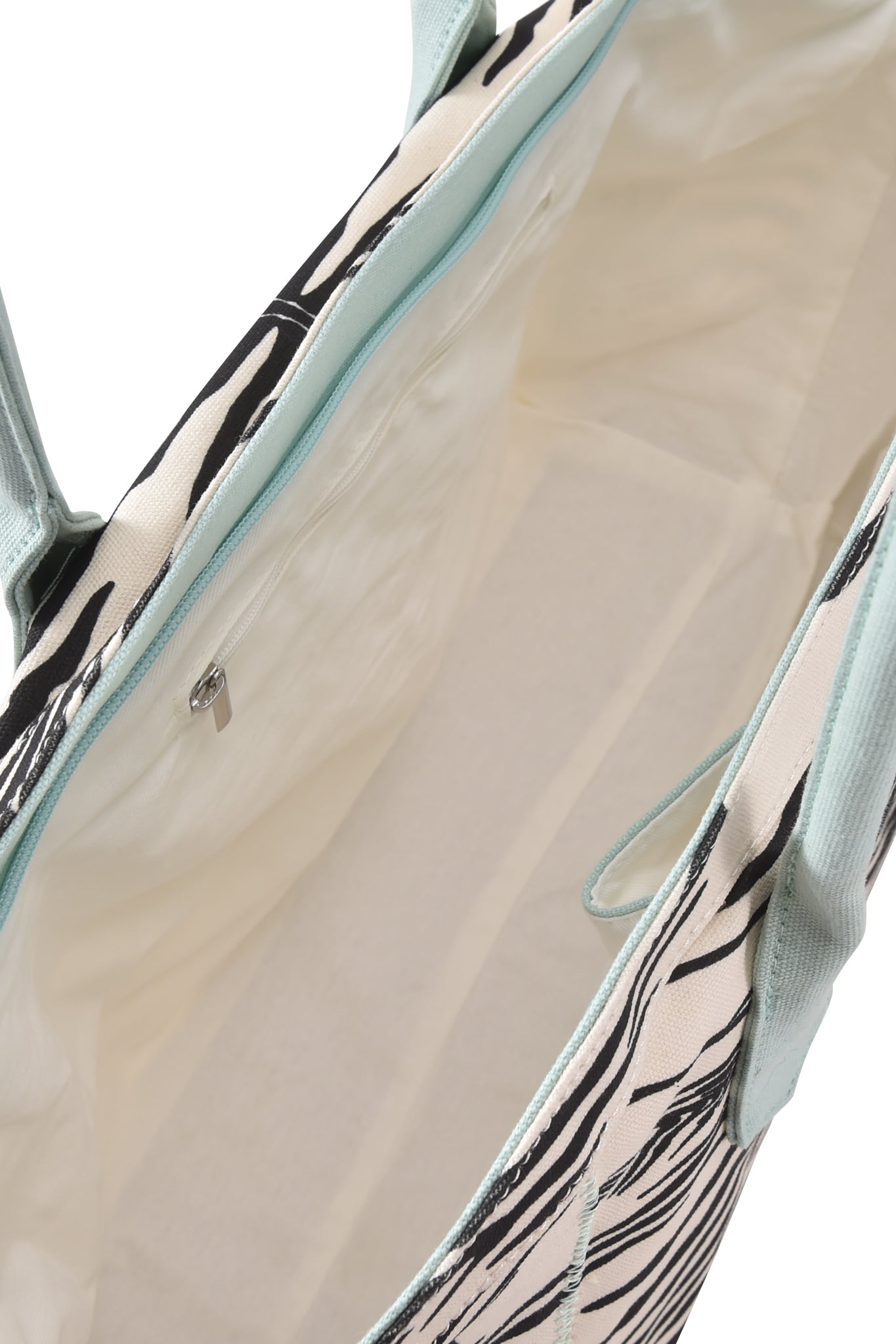 Introducing the BLARE TOTE BAG - FINE LINE ZEBRA by I.AM.GIA: An oversized shopper bag crafted from heavyweight cotton canvas, featuring a light-colored interior with a small zippered pocket and sturdy light blue handles. The exterior boasts an abstract interpretation of the classic black and white zebra print, making this tote bag bold and distinctive.