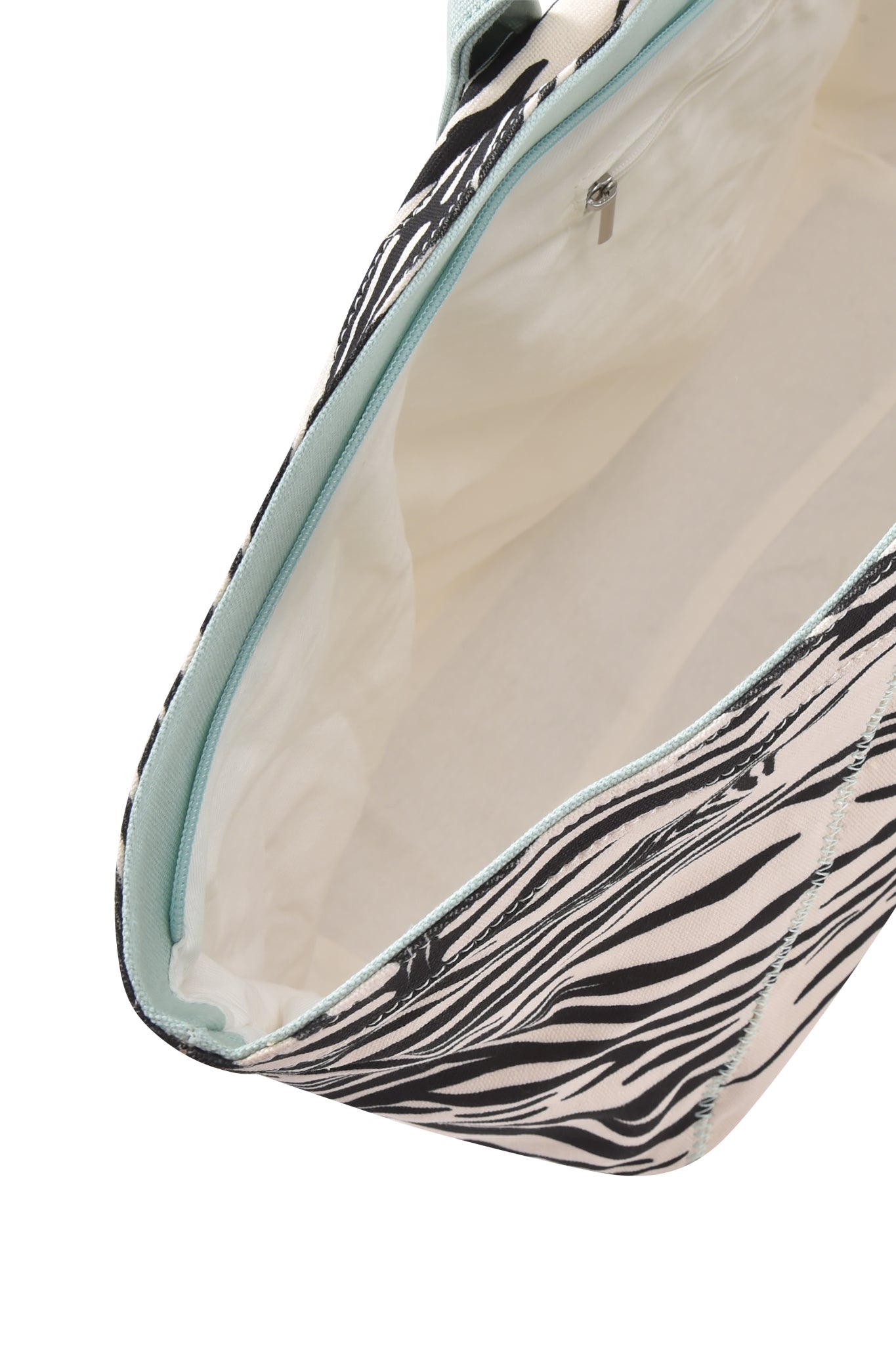 A close-up view of the BLARE TOTE BAG - FINE LINE ZEBRA by I.AM.GIA, crafted from heavyweight cotton canvas with a striking black and white zebra print exterior, a light-colored interior, and featuring an inside pocket and zipper.