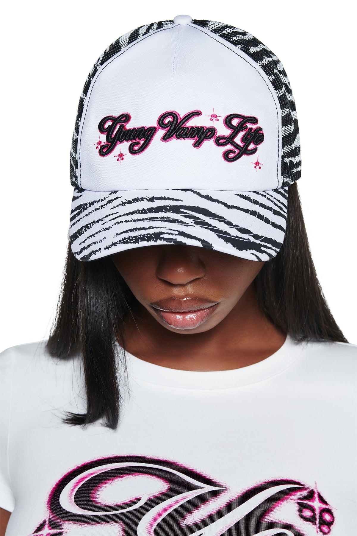 A person wearing an I.AM.GIA YVL TRUCKER HAT - ZEBRA, featuring a zebra-print design with the words “Young Vamp Life” embroidered in pink and black on the front.