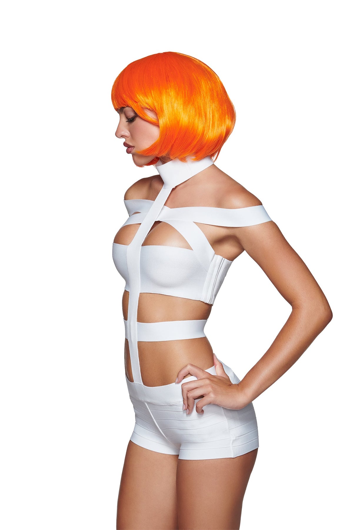 A woman stands in profile against a plain white background, wearing a futuristic white strappy outfit and the QUINTA WIG - ORANGE by I.AM.GIA—a bold synthetic wig that adds the perfect sci-fi edge to her striking look.