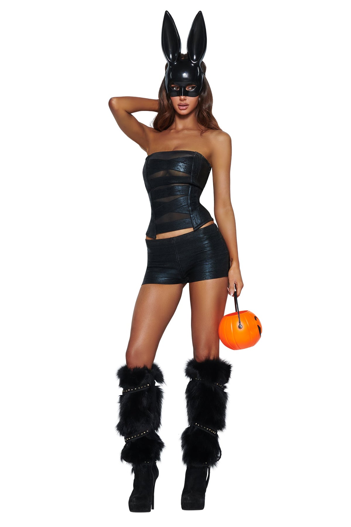 A woman wearing a black strapless outfit, black furry leg warmers, high heels, and the I.AM.GIA DOE BUNNY MASK - BLACK—an eye-catching Halloween costume accessory—holds a small orange pumpkin bucket.