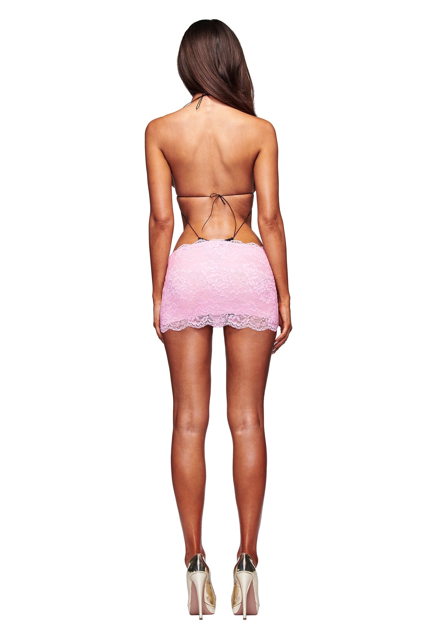 A woman with long brown hair stands with her back to the camera, wearing the black AMBER LACE BODYSUIT by I.AM.GIA. The backless bodysuit features thin straps and lace details, paired with high heels against a plain white background.