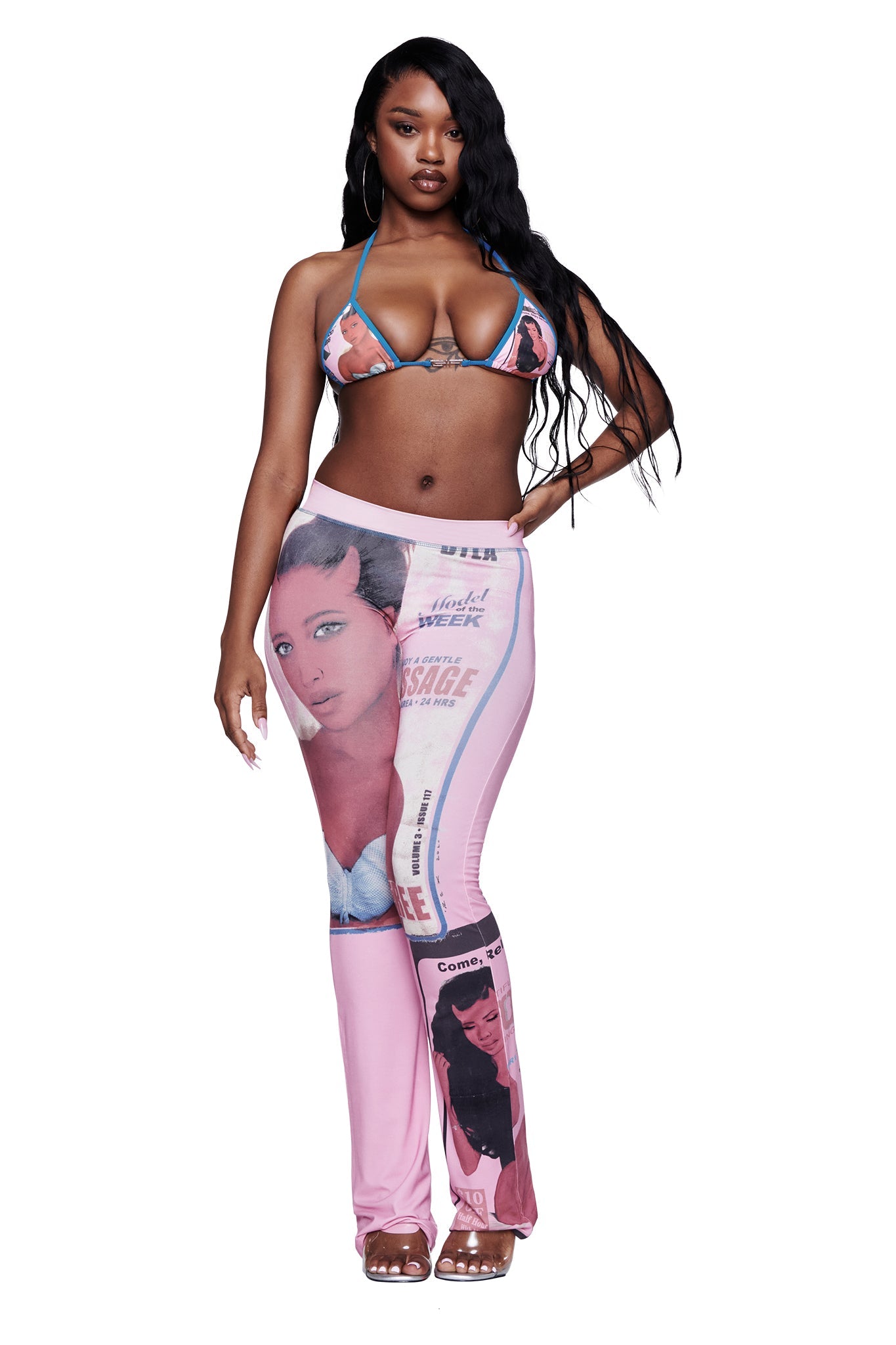 A woman with long black hair wears the I.AM.GIA T-REX AVA BIKINI TOP in pink, paired with pink pants featuring large, vintage-style newspaper and portrait prints, standing against a white background.
