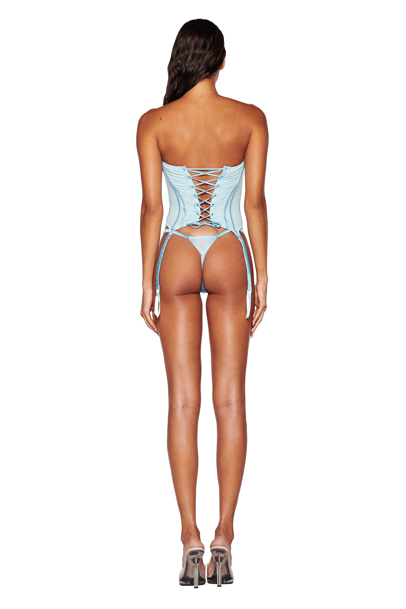 A rear view showcases a person in the ANGELIQUE BUSTIER SET - BLUE : BABY BLUE by I.AM.GIA, featuring lace-up detailing and garter straps. The stunning ensemble is paired with high heels and set against a plain white background, which emphasizes the corset's intricate design.