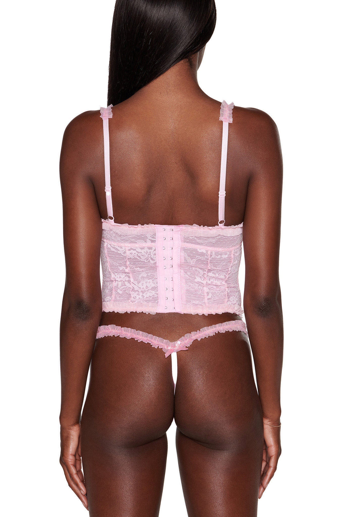 A back view displays someone wearing the MADISON BUSTIER - PINK from I.AM.GIA, paired with matching lingerie bottoms. This pink lace bustier showcases intricate details and adjustable shoulder straps, set against a white background.