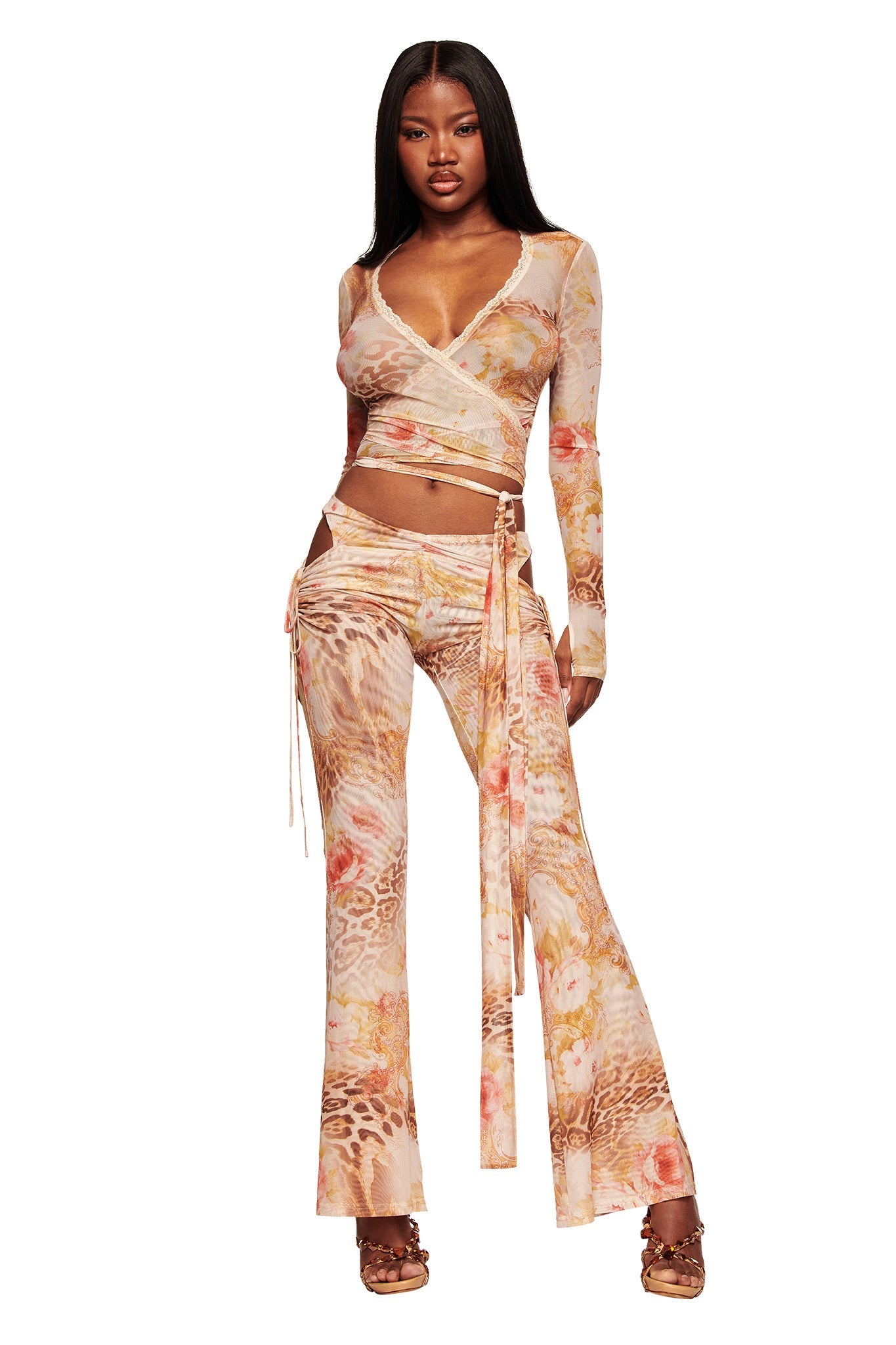 A woman models the ERISKA TOP - DESERT ROSE by I.AM.GIA, a sheer mesh wrap top paired with matching high-waisted flared pants in a peach, orange, and tan floral animal print. She finishes the look with heeled sandals.