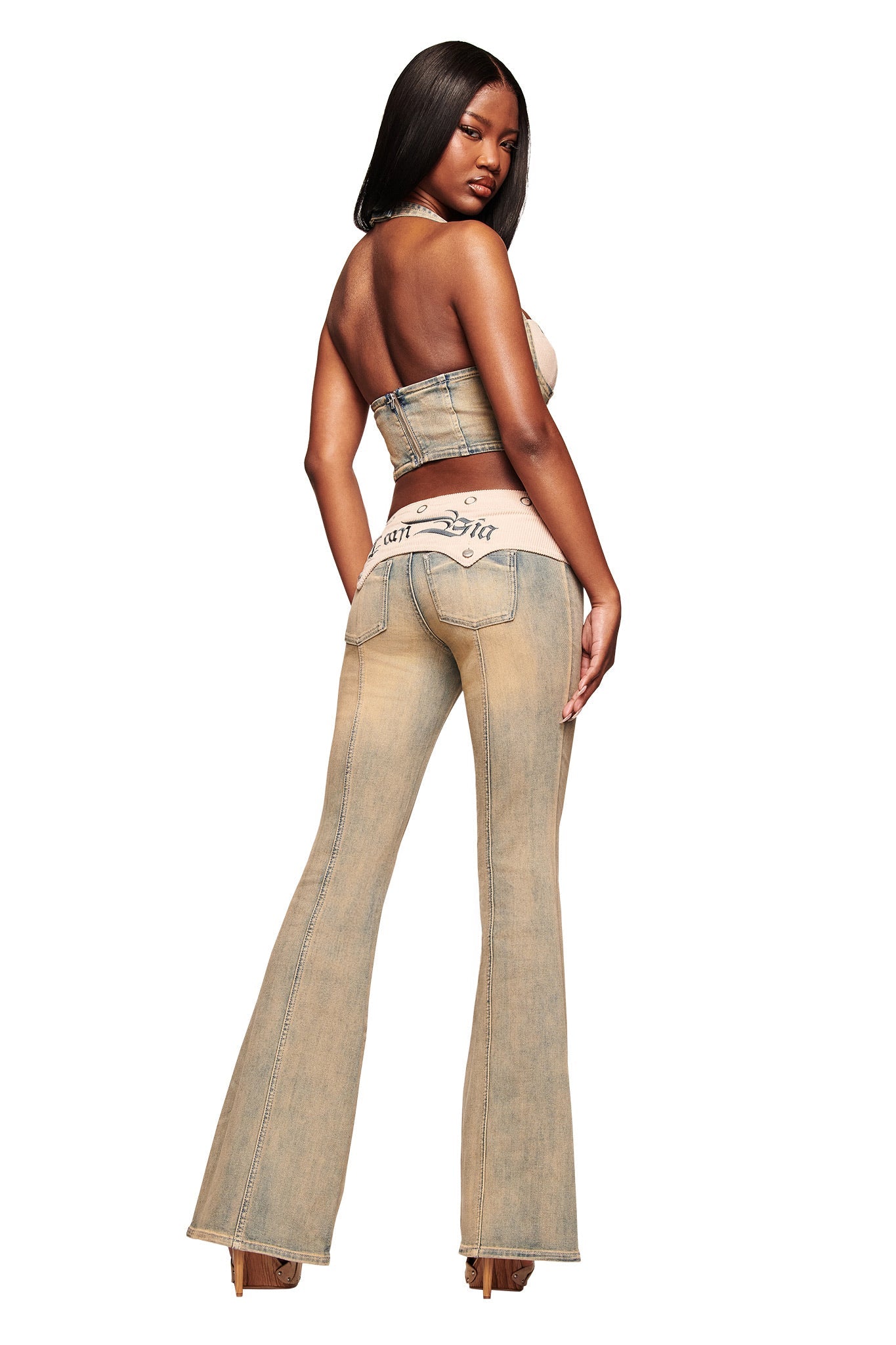 A woman with long dark hair models the I.AM.GIA TOMMIE JEAN - ANTIQUE DENIM light-wash, mid-rise flared jeans and a matching strapless top, standing sideways and looking back over her shoulder against a white background.