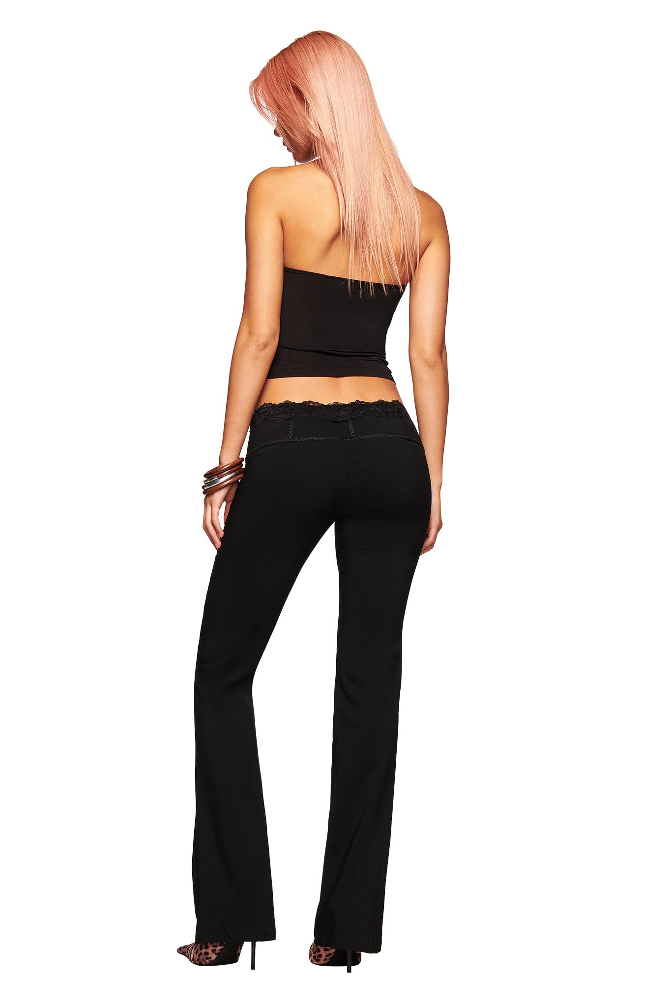 A woman with long pink hair stands facing away from the camera against a white background. She wears a black strapless top, high heels, bracelets, and the I.AM.GIA SERAYA PANT - BLACK: mid-rise stretch woven pants with lace trim.